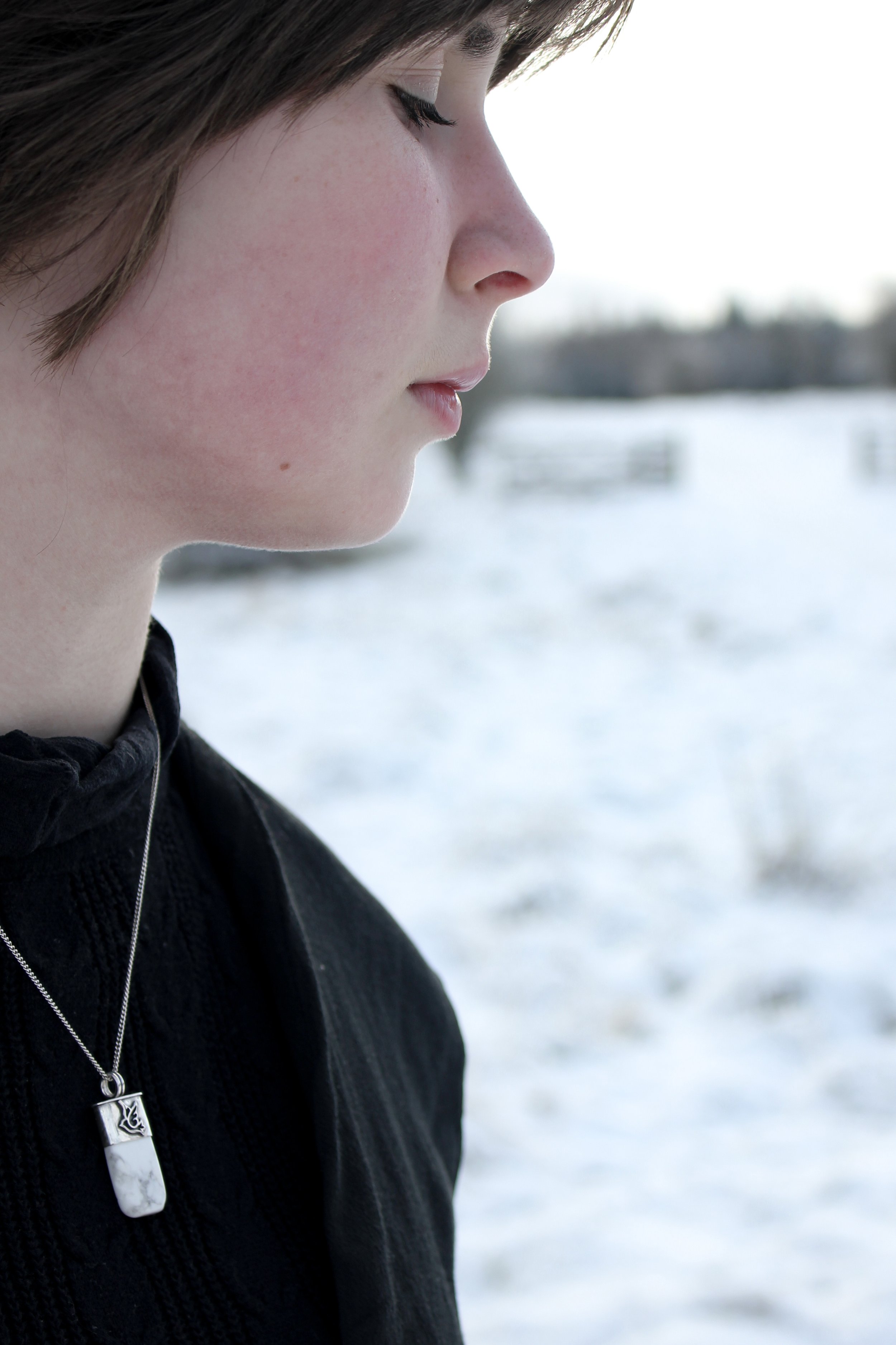 Model in black top against a snowy landscape, her eyes closed in contemplation. The silver dove talisman is around her neck, the white and grey pattern of the howlite echoed in the backdrop.
