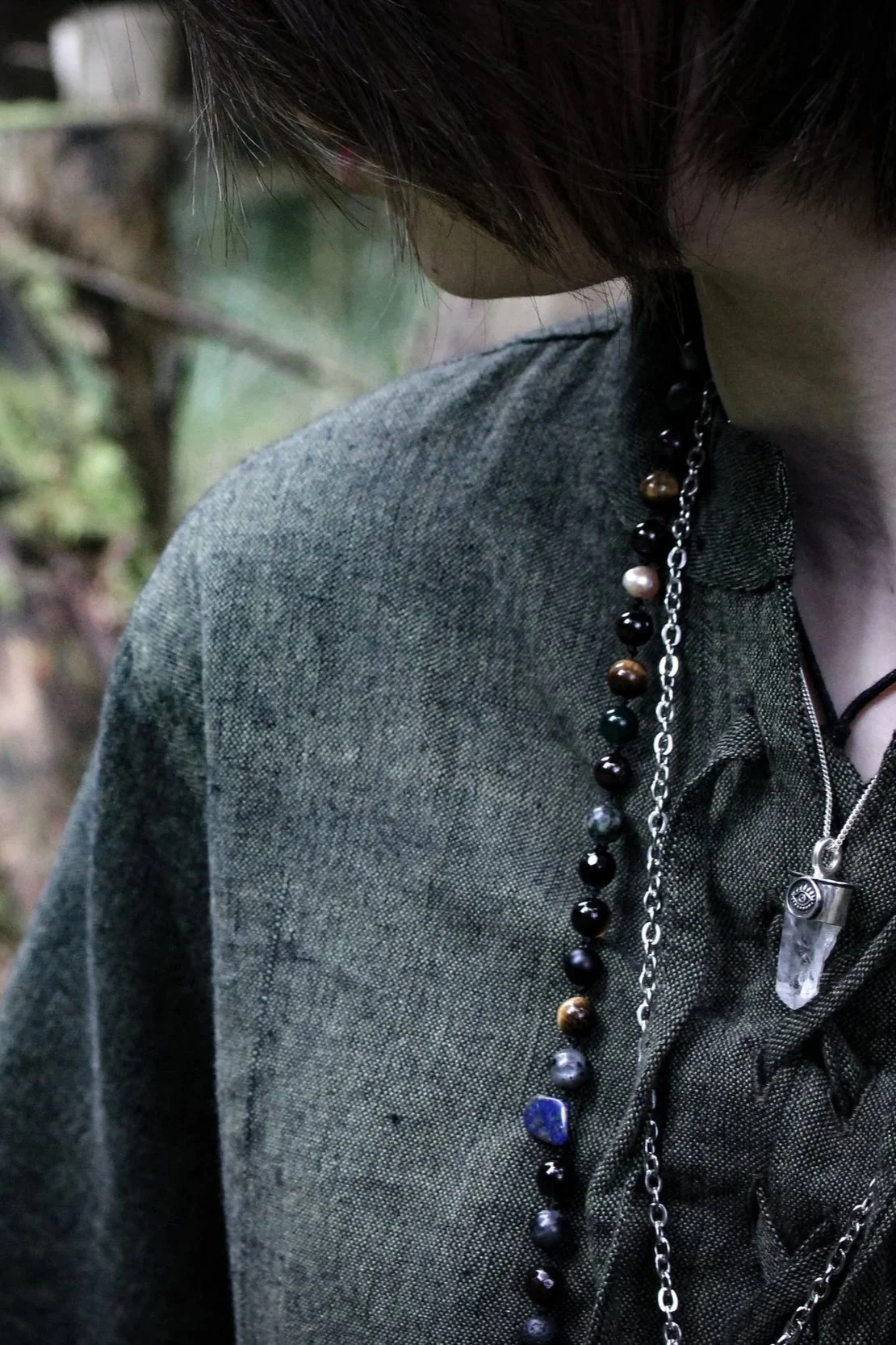 Model in a green shirt in a forest with a beads around her neck and a silver and rough quartz point pendant with an eye motif worked in the silver