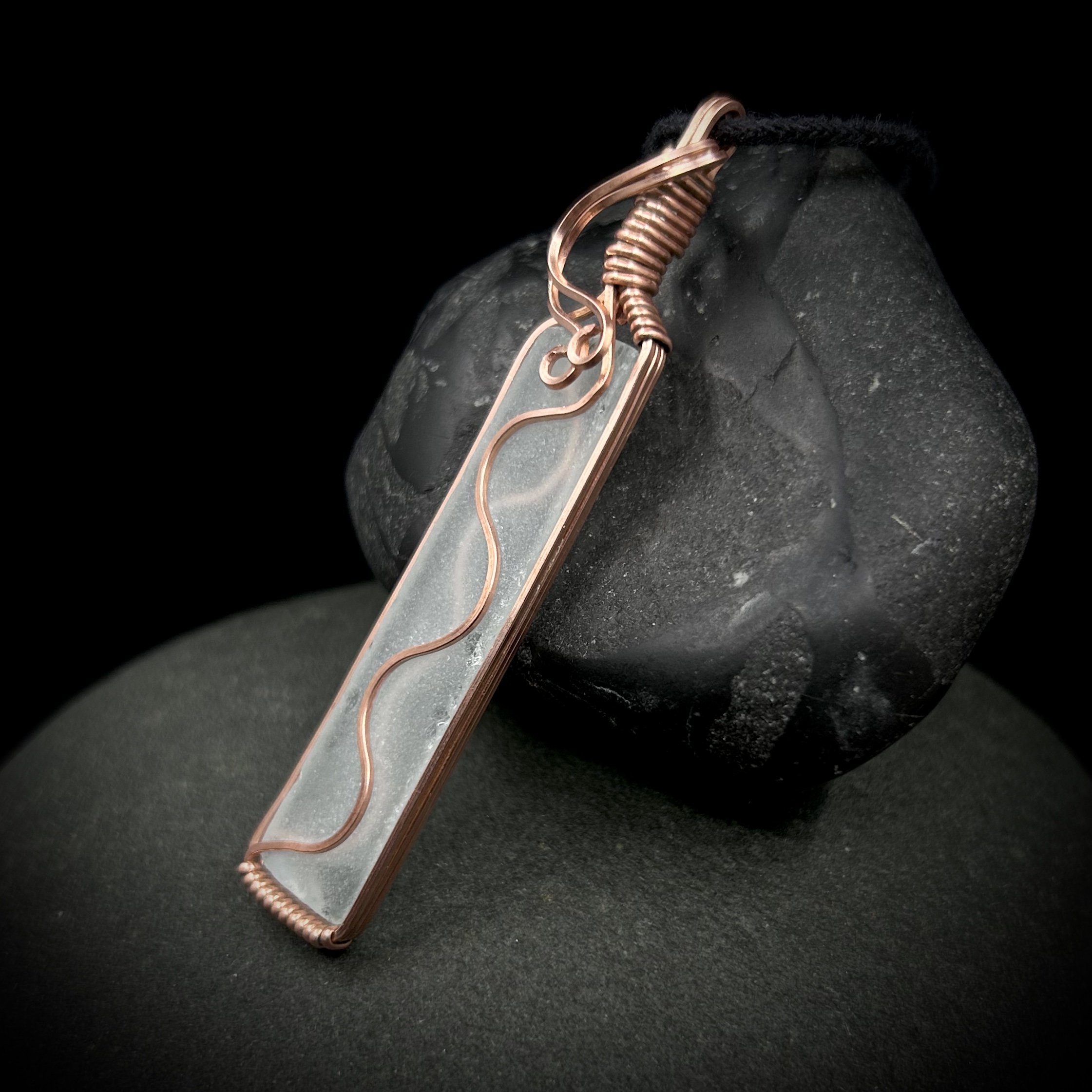 Long, thin rectangular clear sea glass wrapped in bright copper with swirls and waves running on both sides of the transparent glass