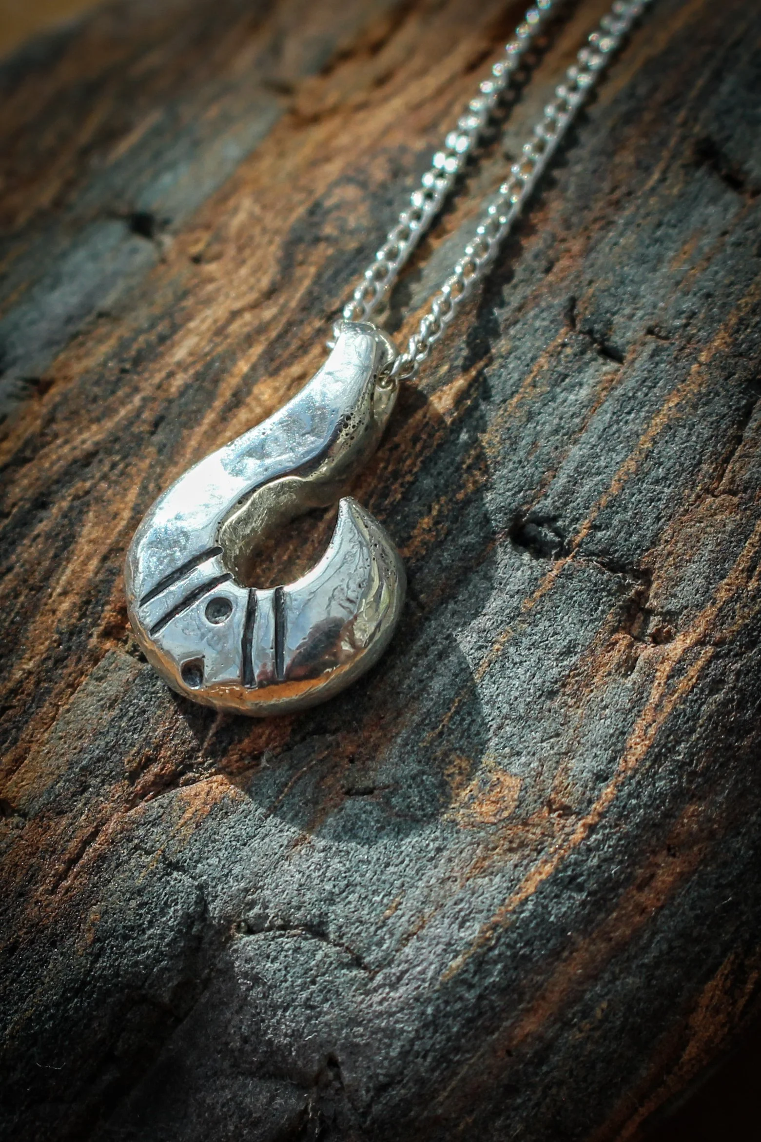 Abstract silver flame pendant lying on a fire coloured rock. The silver is polished and shiny and bears a decoration of 11:11 on its curve. 