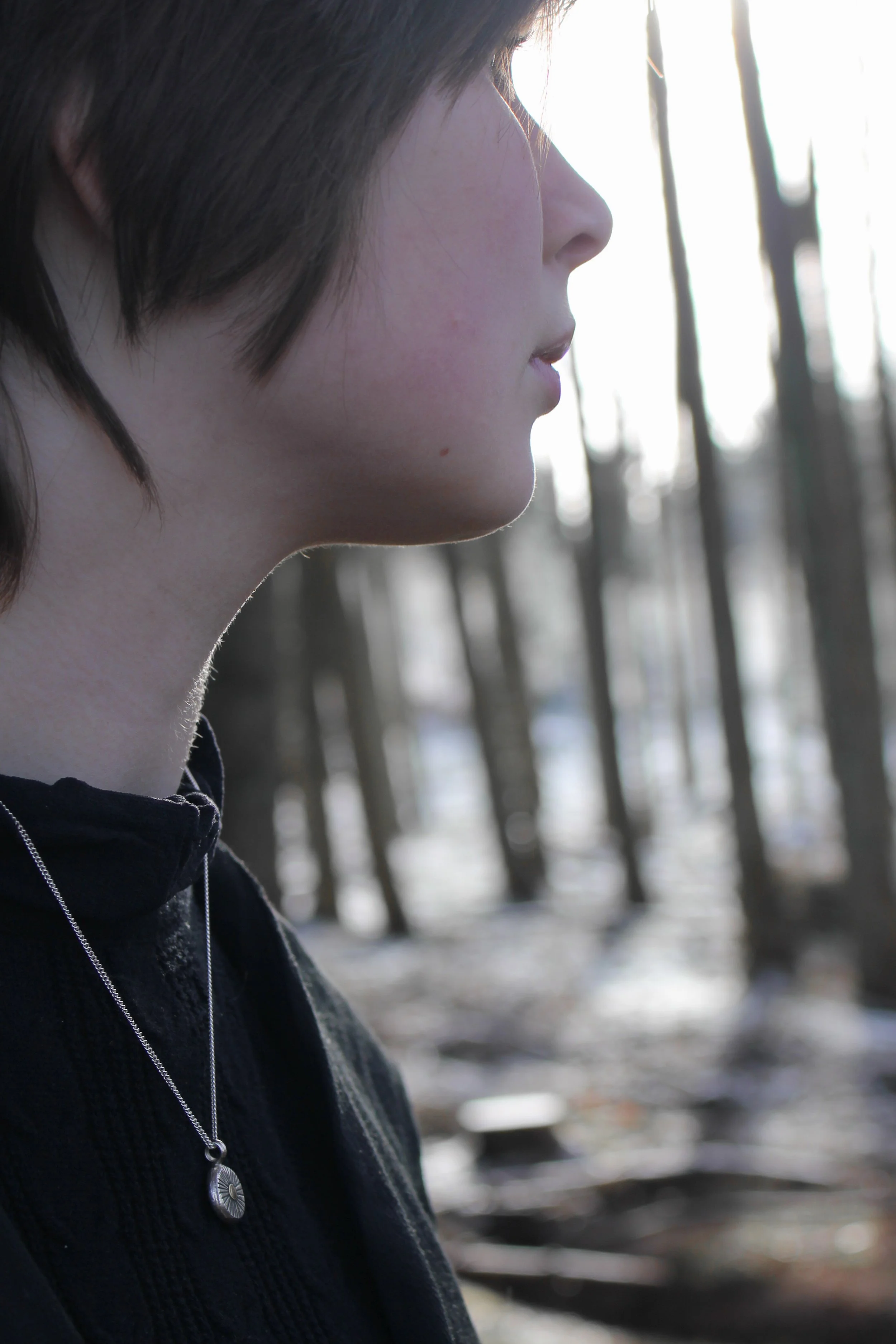 Model wearing silver and gold ancient goddess pendant against a black top in a bare, snowy woodland