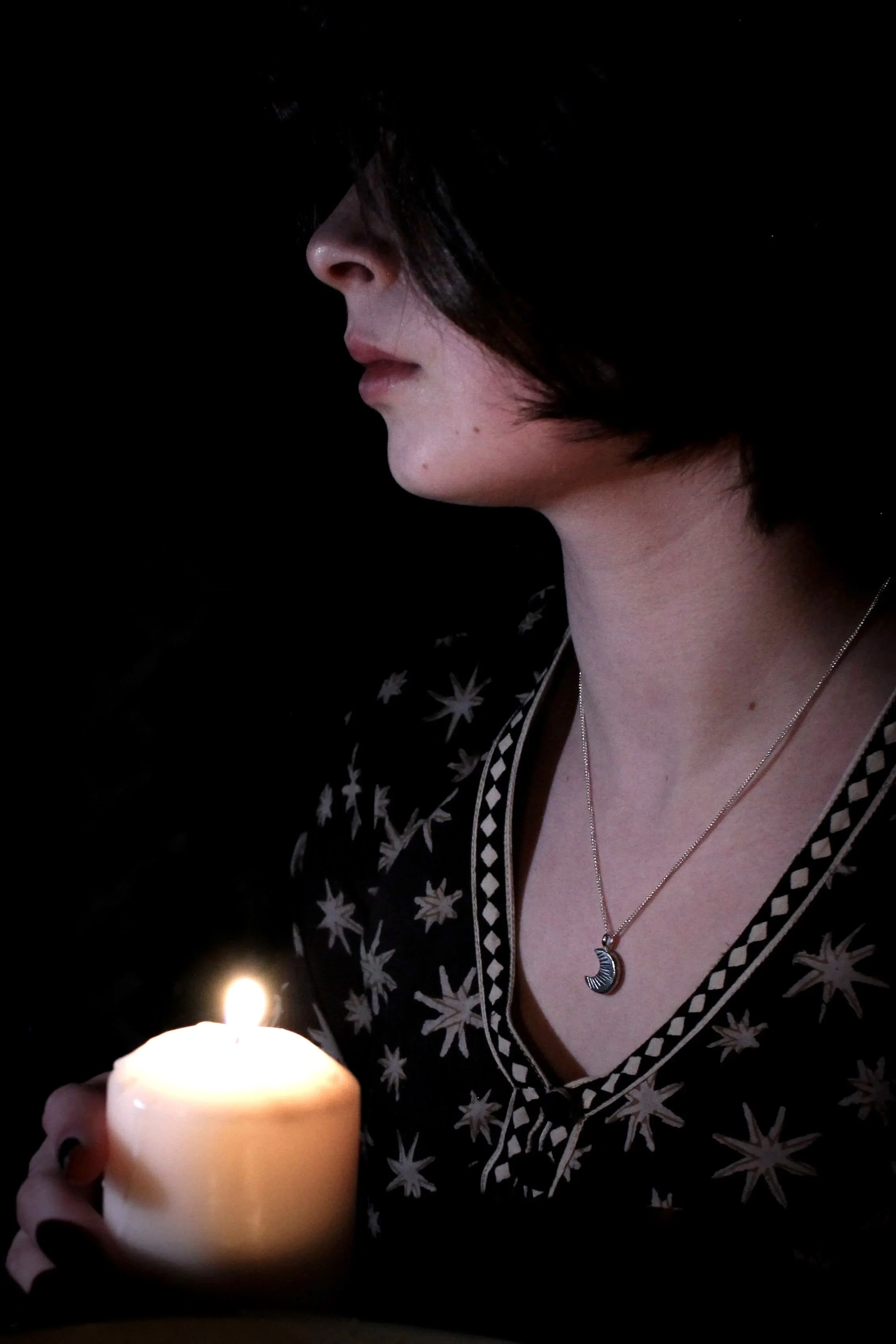 Model in a black star print dress bathed in candlelight wearing a silver crescent Laussel moon pendant around her neck