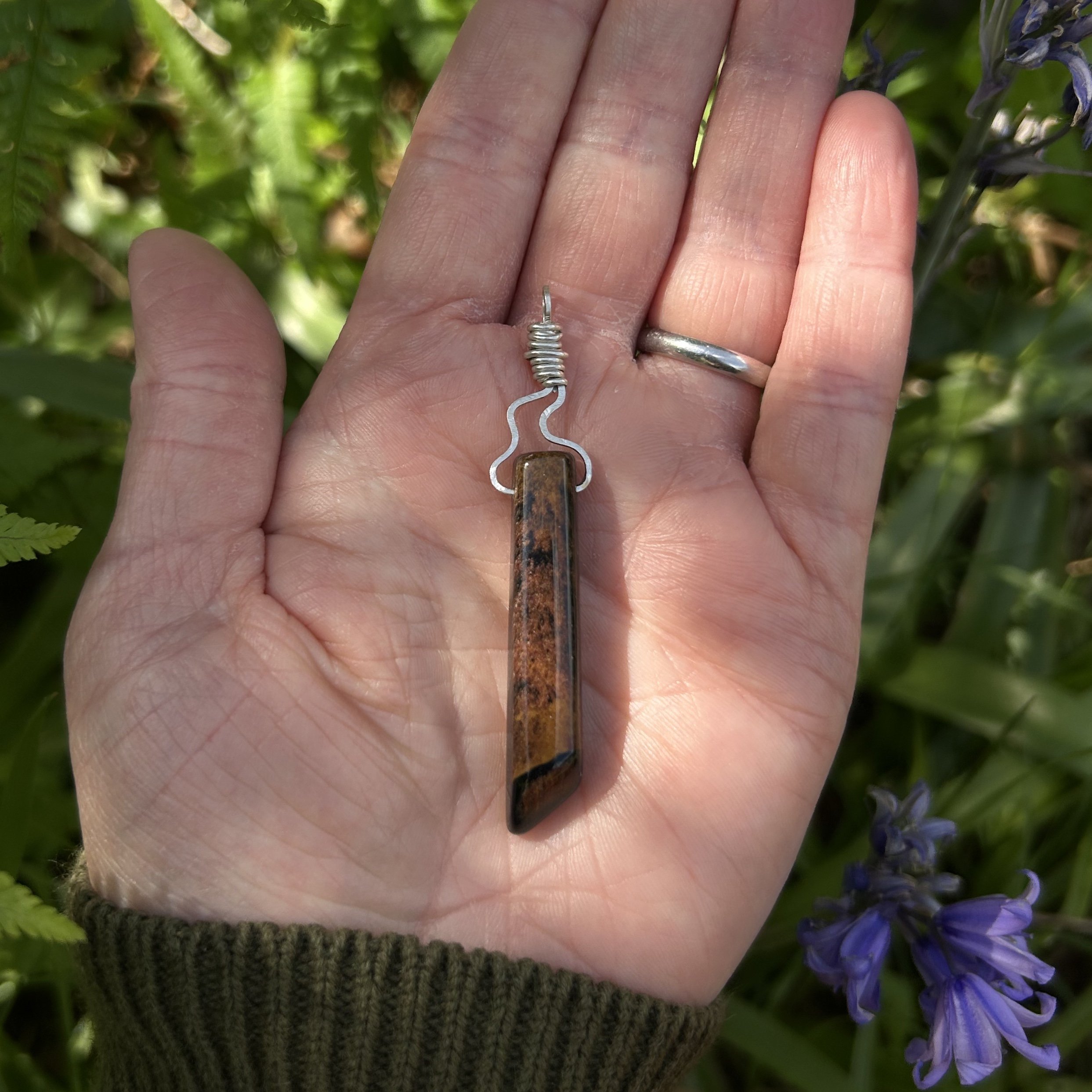 Tiger eye pendant with silver flame bail detail on women’s palm, the dappled sunlight highlighting the warm brown tones of the crystal.