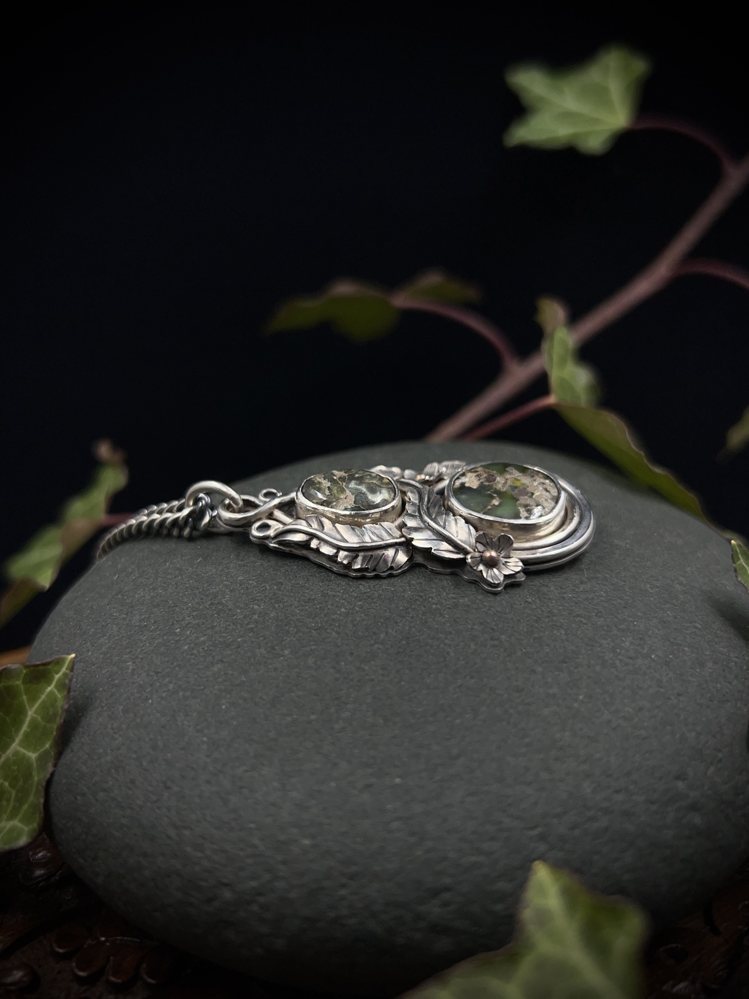 A close up on the handmade leaf and flower details from the silver pendant, highlighting the 9ct rose gold centres to the flowers