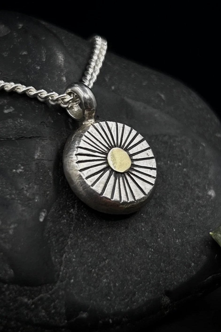 Close up of rustic sun design pendant in silver, stamped with irregular lines and solid gold disc in center