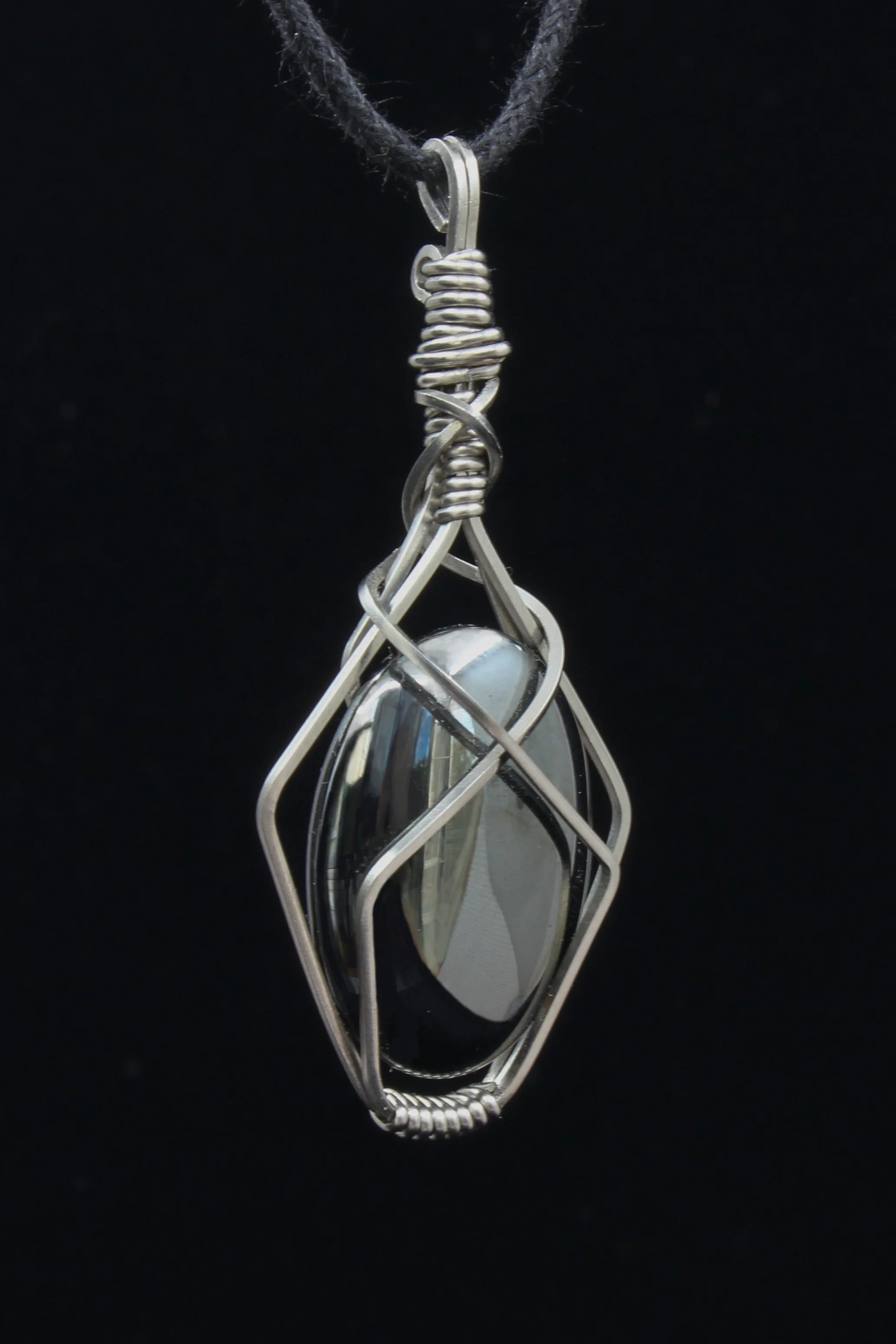Close up of hematite and steel wrapped pendant showing the details of steel wire wrap and the mirror finish of the hematite stone