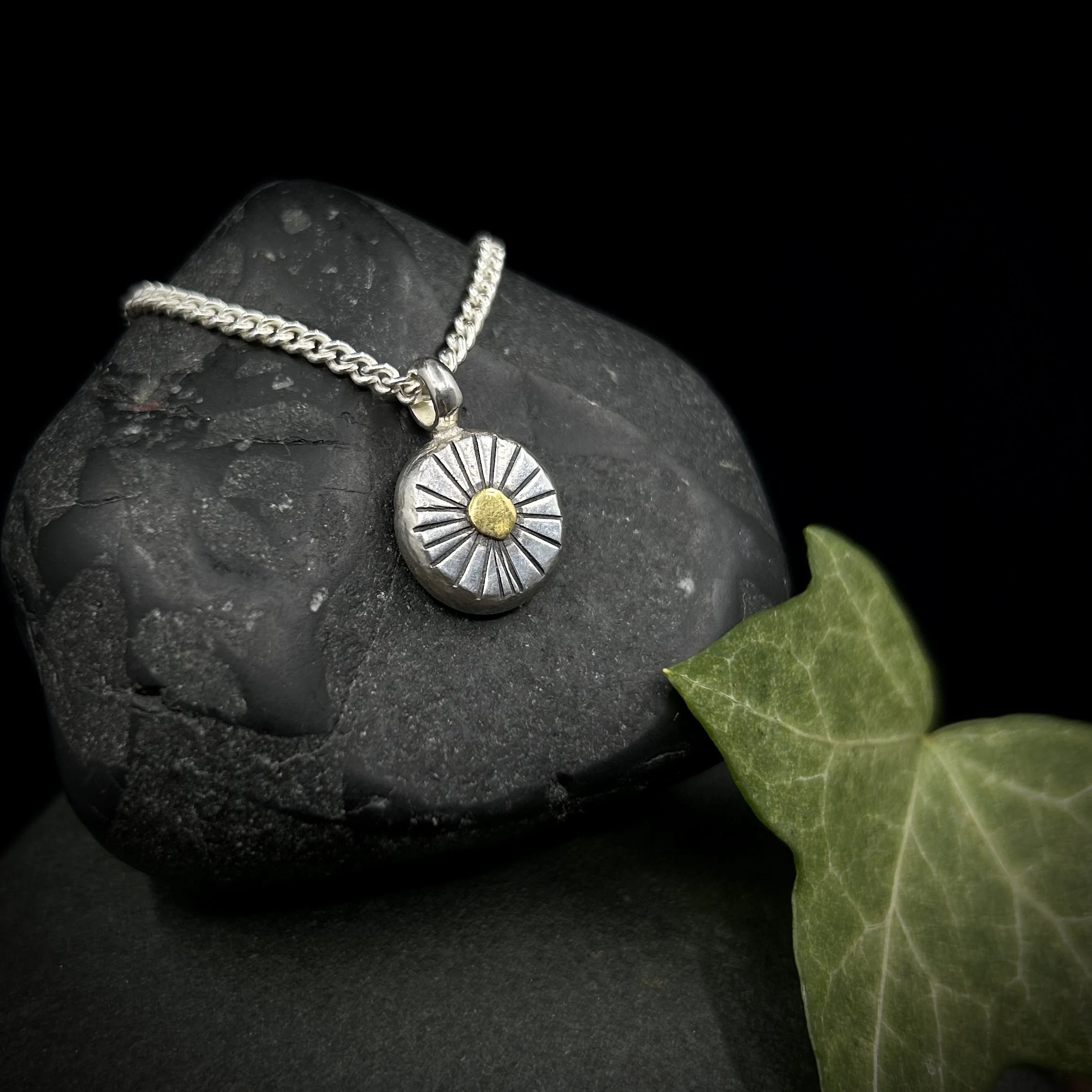Side view of sun pendant showing the thickness of the silver, the deep texturing lines radiating out from the 24k gold disc and the silver curb chain