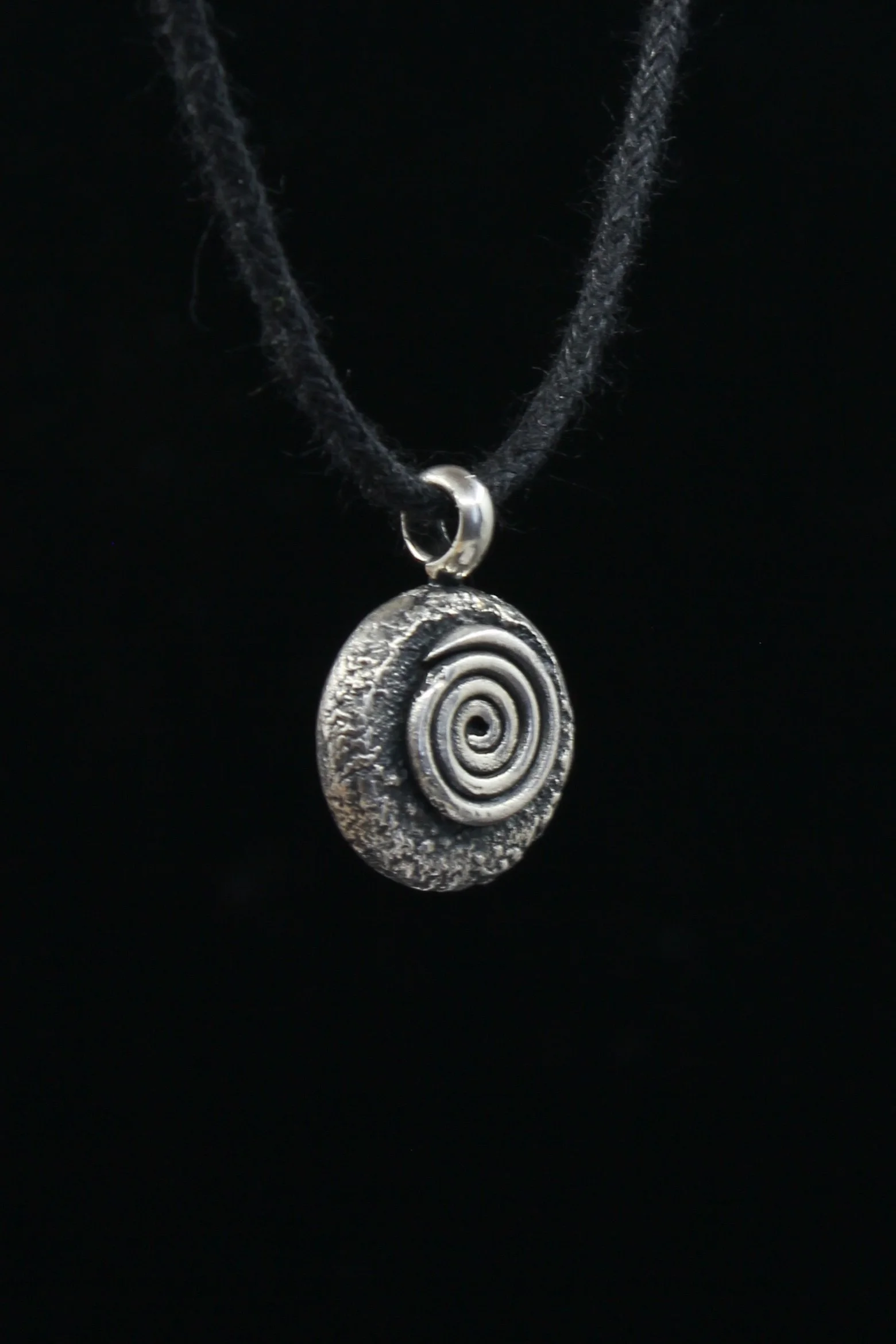 Side view of round spiral pendant showing thickness of silver and heavily textured detail