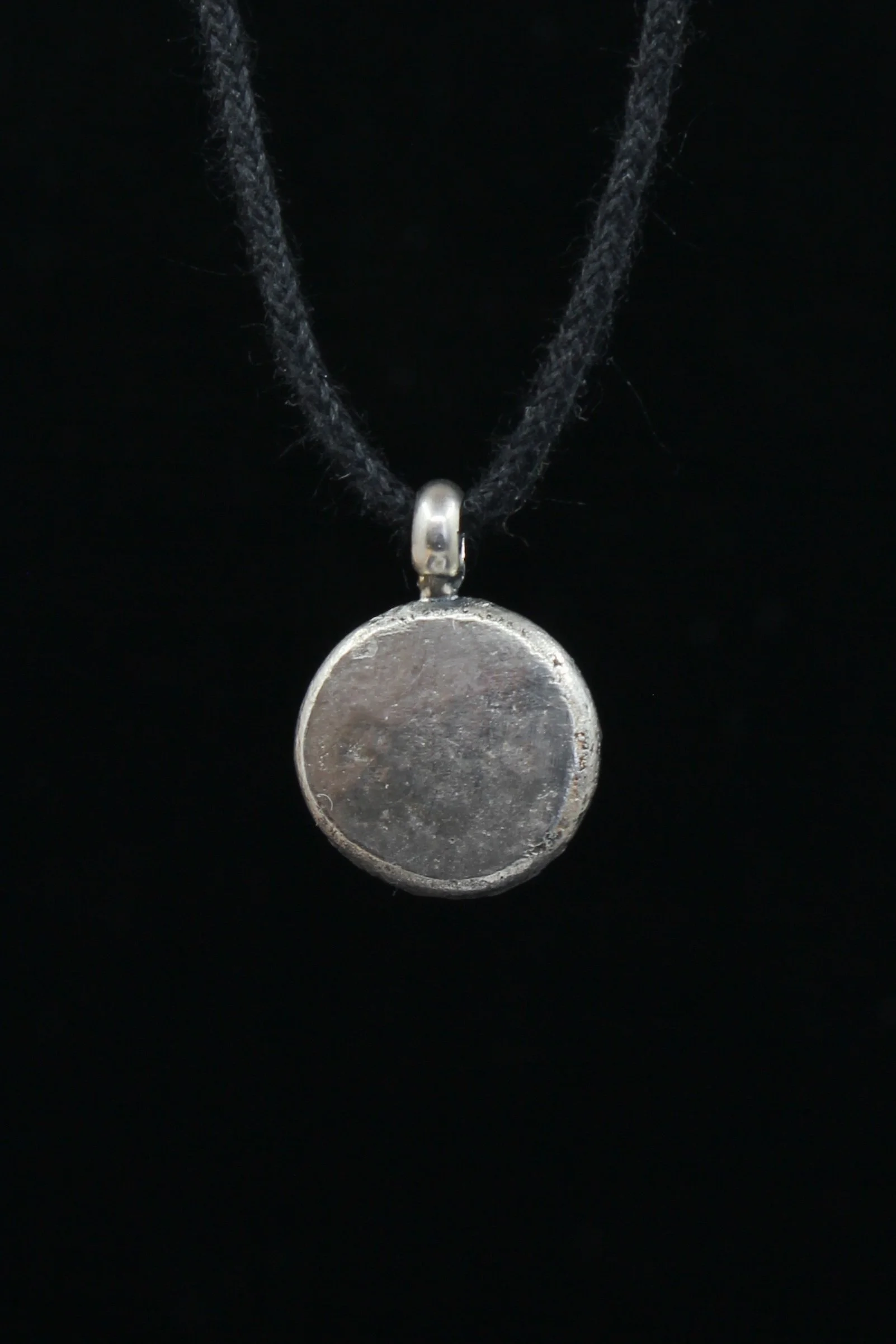 Back view of round spiral pendant showing a smooth silver surface with marks of hand forging remaining