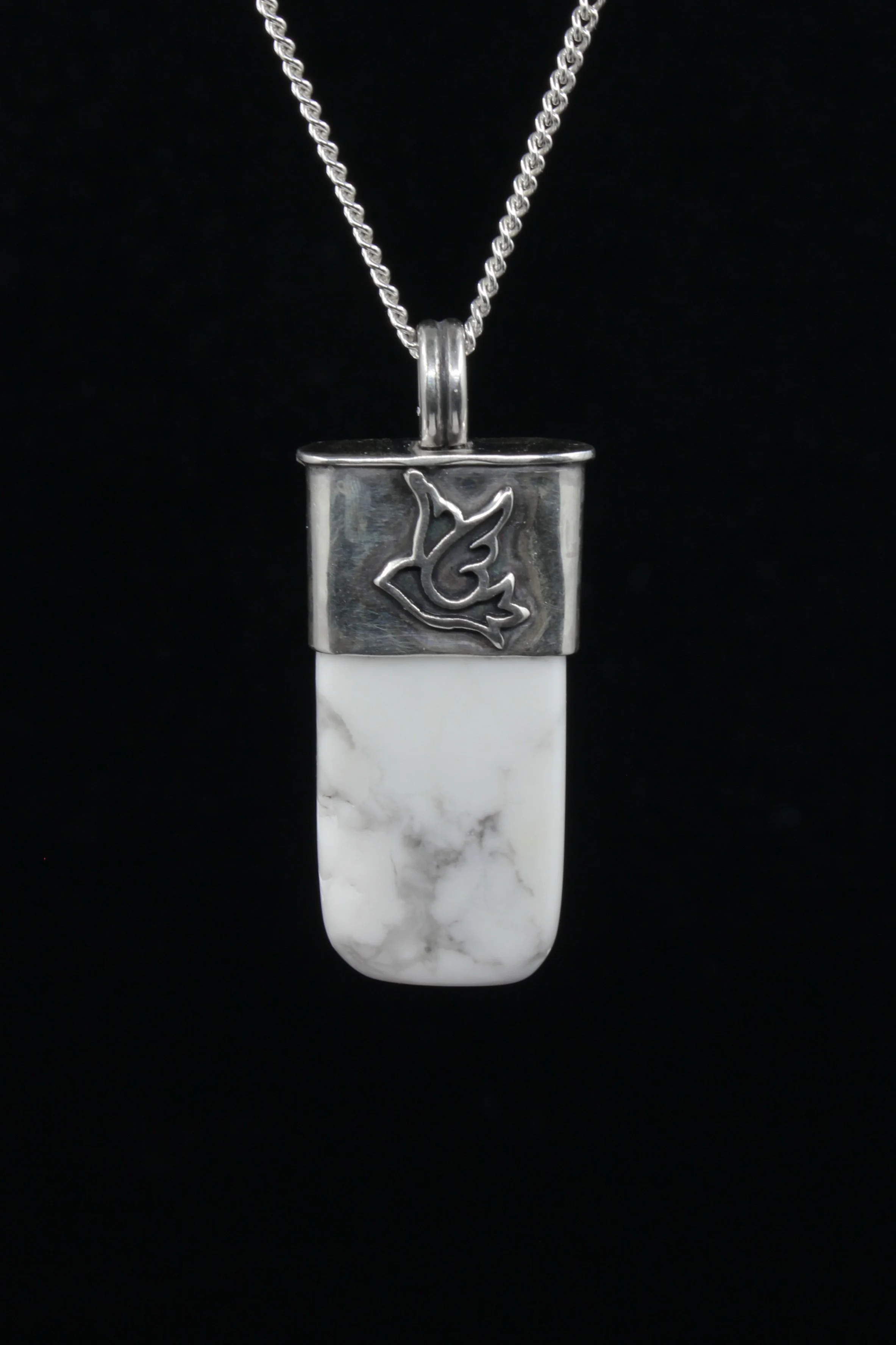 A silver and white howlite rectangular talisman with a silver motif of a dove mid-flight on the silver setting