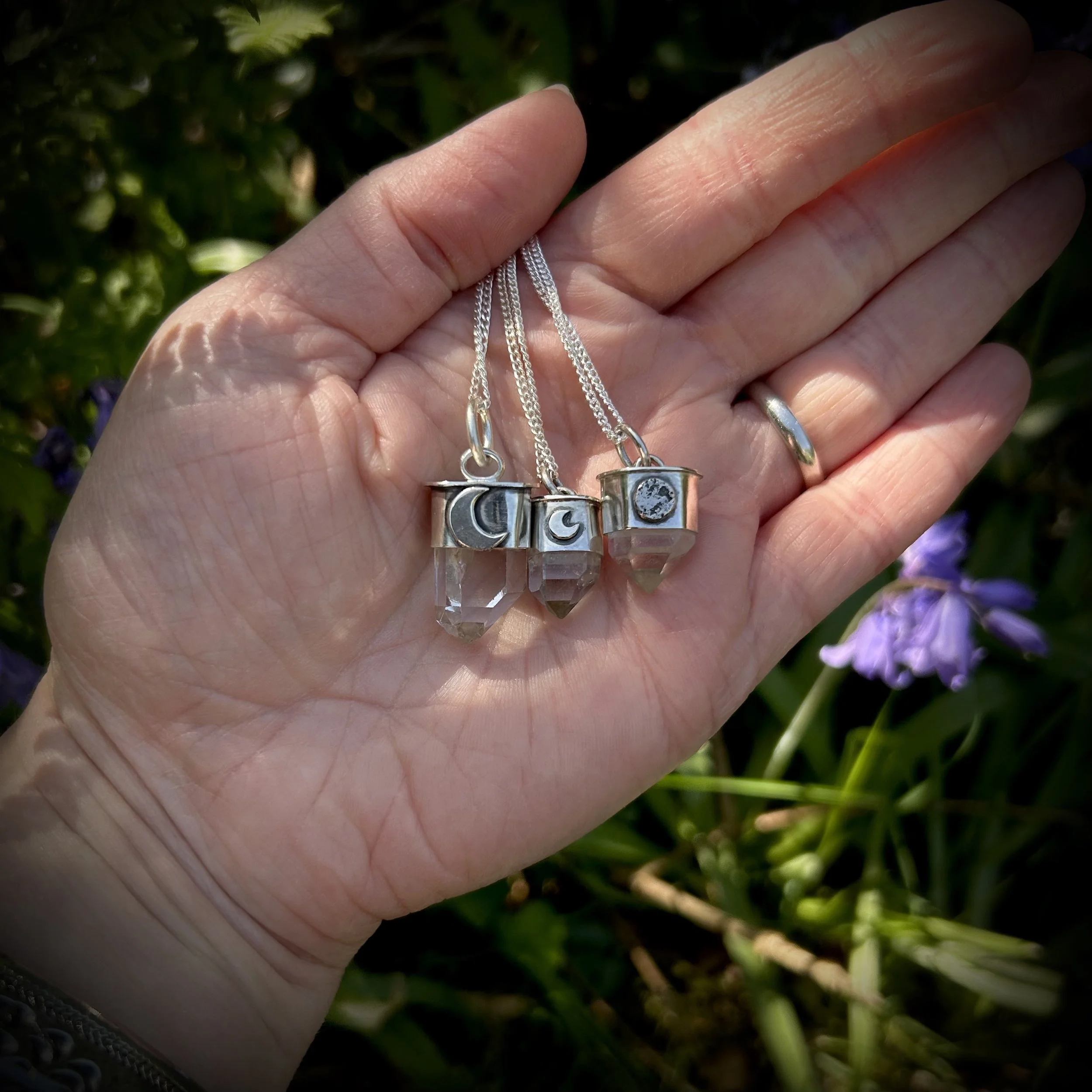 A women’s palm revealing three silver quartz moon pendants, two mini and one small for size comparison