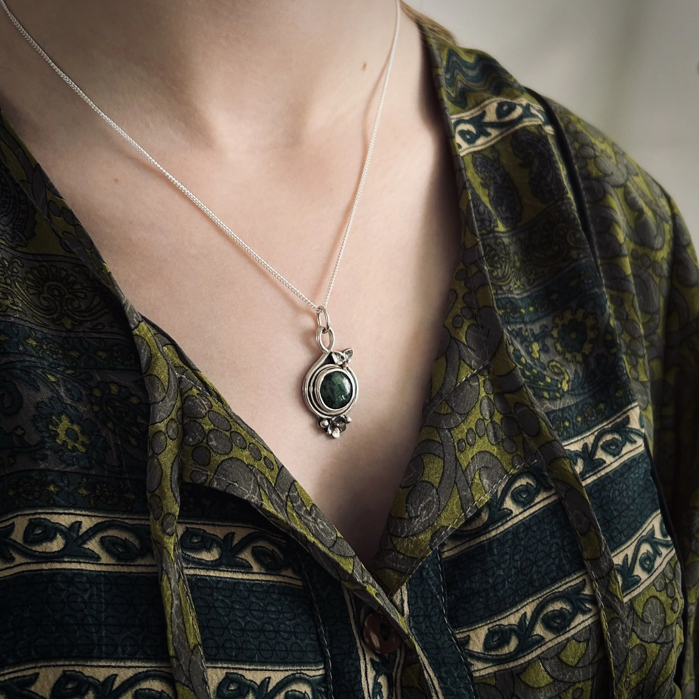 Model in green blouse wearing silver and green zoisite floral pendant on a delicate silver chain