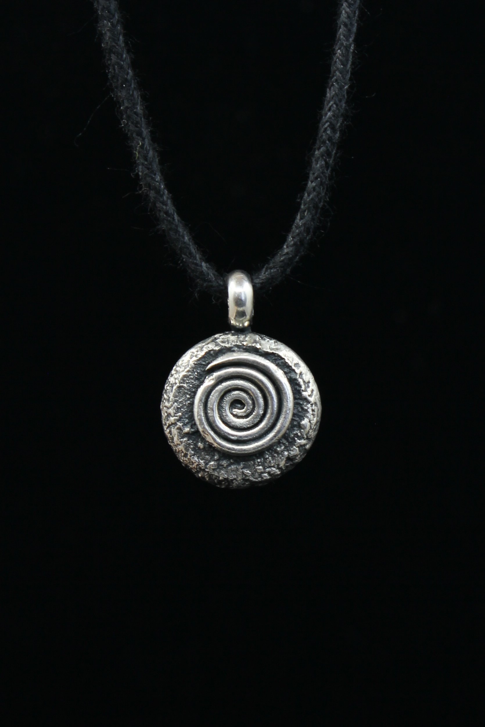 Round heavy textured and oxidised silver pendant with raised spiral design on black cord