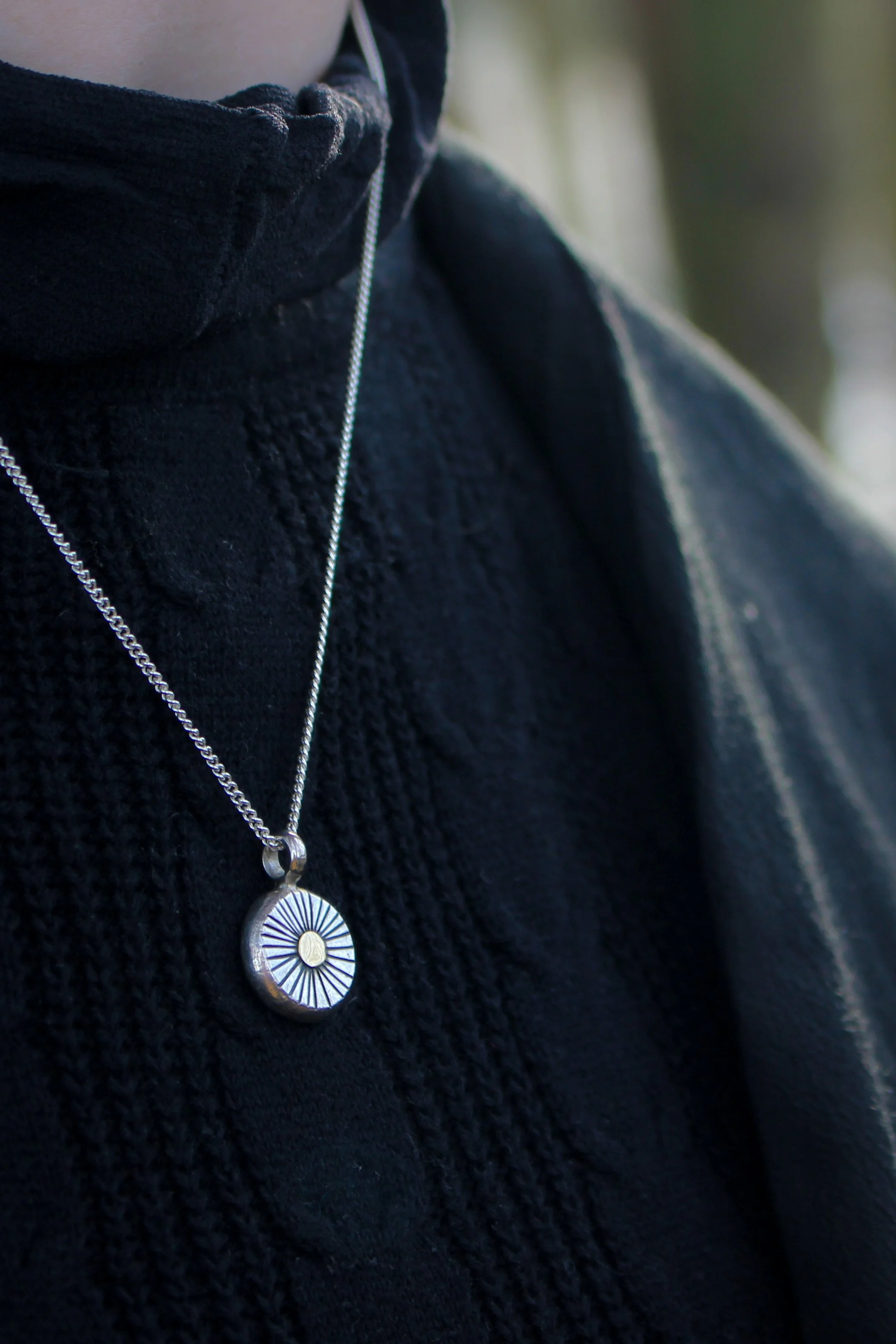 Close up of model wearing a silver and gold ancient goddess sun pendant around her neck. The black top contrasts with the bright metals.