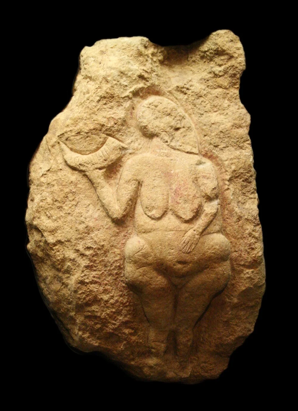 A very old limestone bas relief of a naked woman with one hand on her stomach holding a horn inscribed with thirteen notches aloft in the other hand