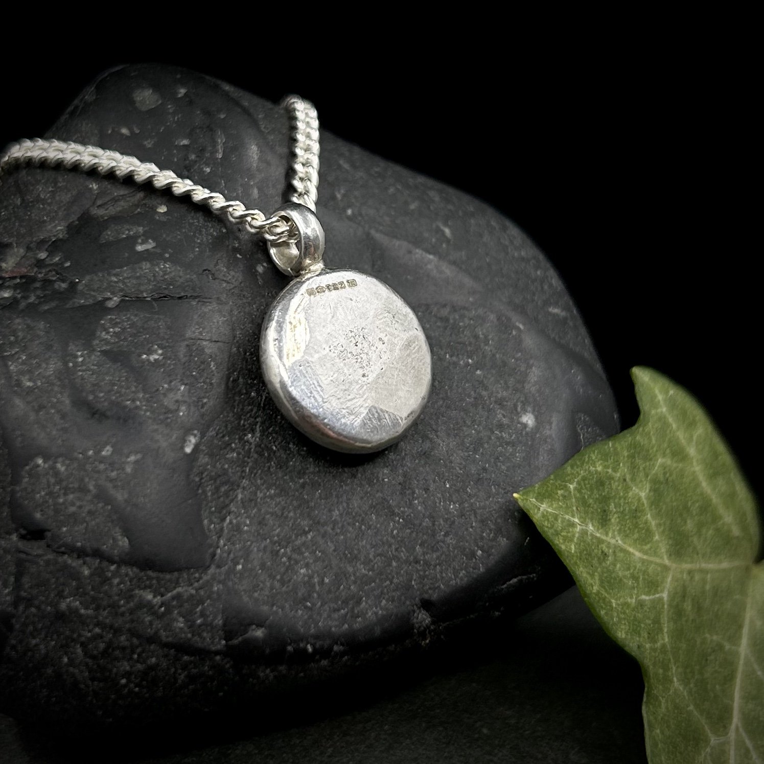 Reverse of solid silver sun pendant showing the textured, hammered back and the full hallmark for silver and gold next to the bail