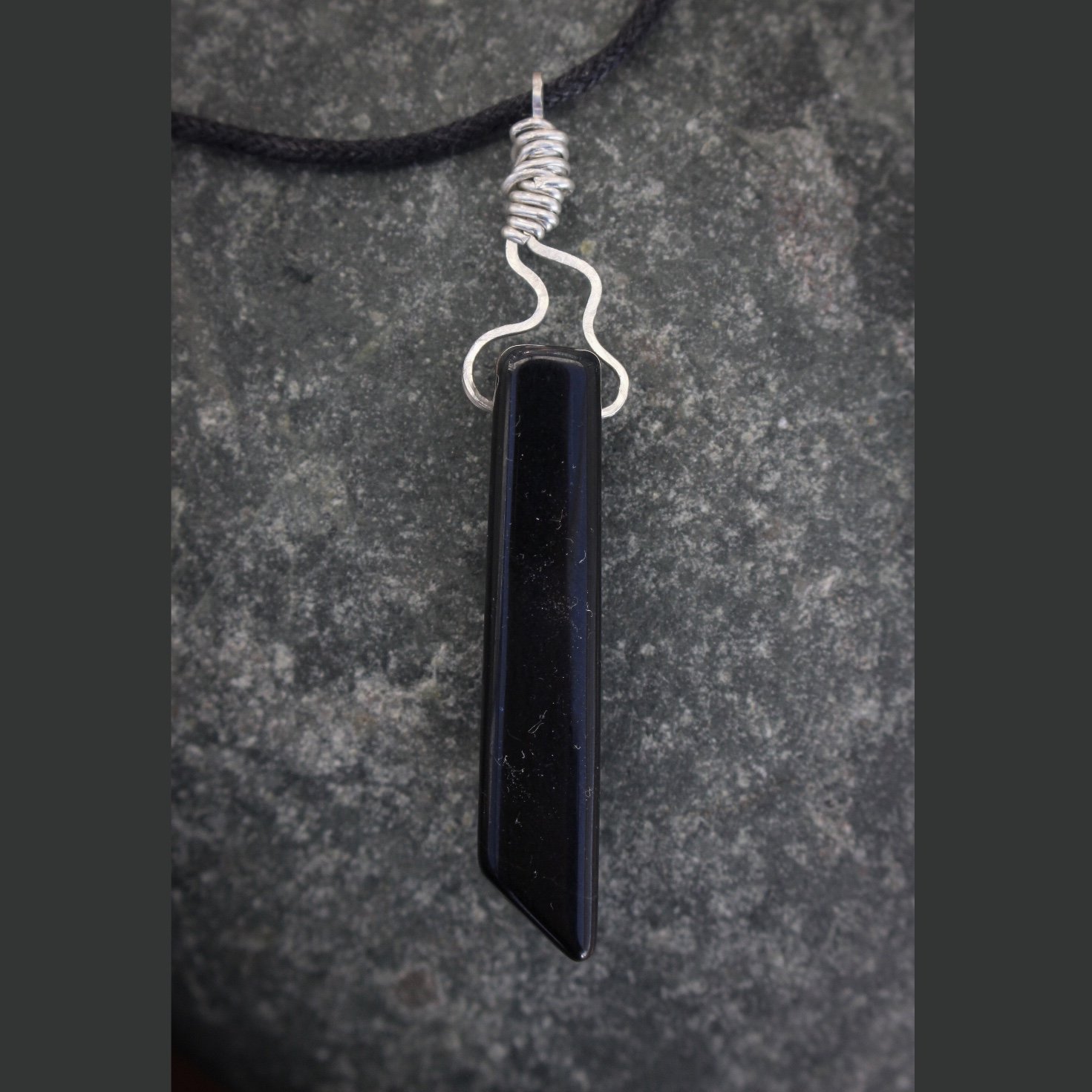 Reverse view of tiger’s eye stone showing a darker side and silver flame tip detail against a slate background