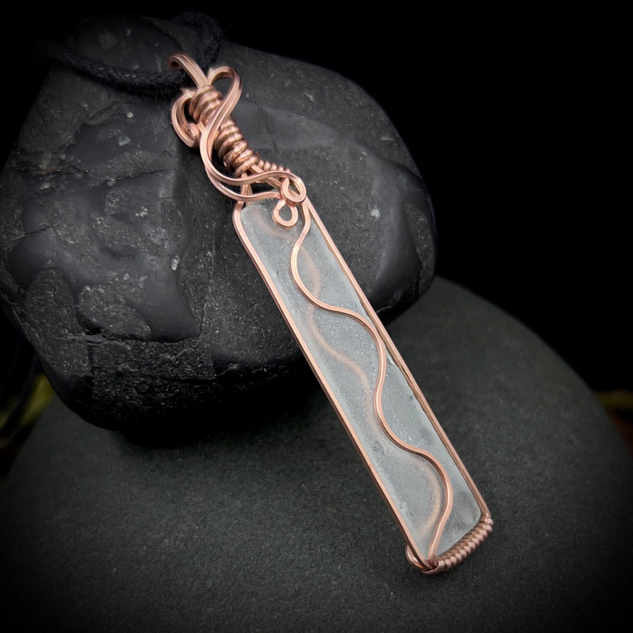 Different view of the bright copper wrapped details on the long, thin transparent sea glass pendant