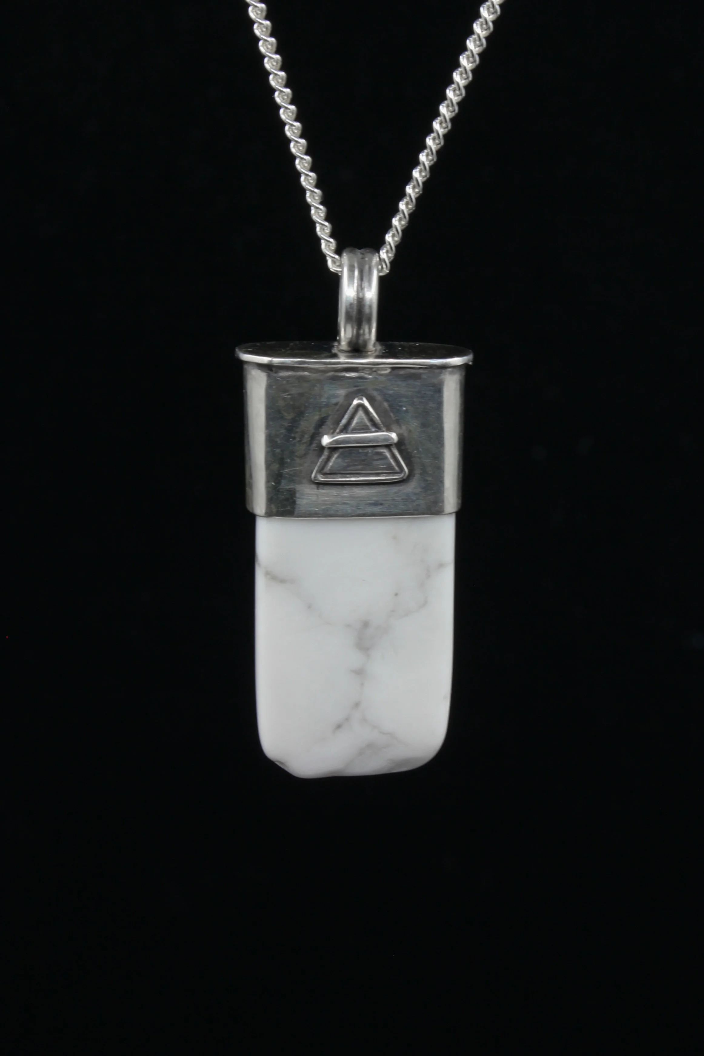 A rectangular white howlite stone set in silver and displaying an upturned triangle with a line through it - the alchemical symbol for Air
