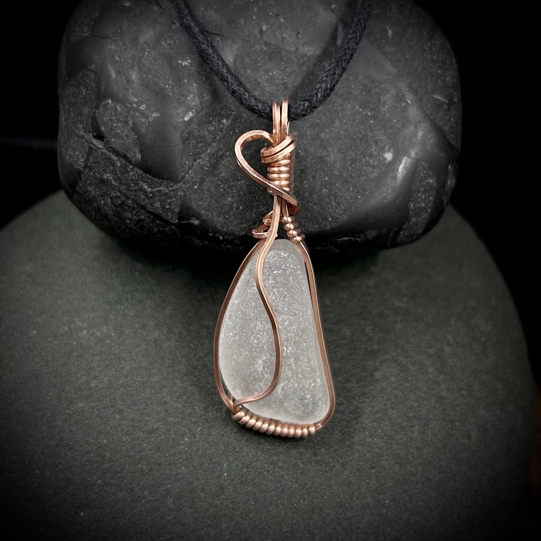 Irregular frosted clear sea glass pendant wrapped in bright copper with abstract wave design and black cord