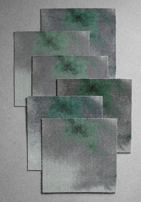 Six watercolor paper sheets with abstract green and black paint splashes arranged on a flat surface.
