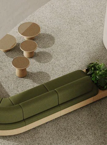 Green upholstered sofa with a wooden base, adjacent to a plant, and three small beige dotted tables on a speckled gray floor.