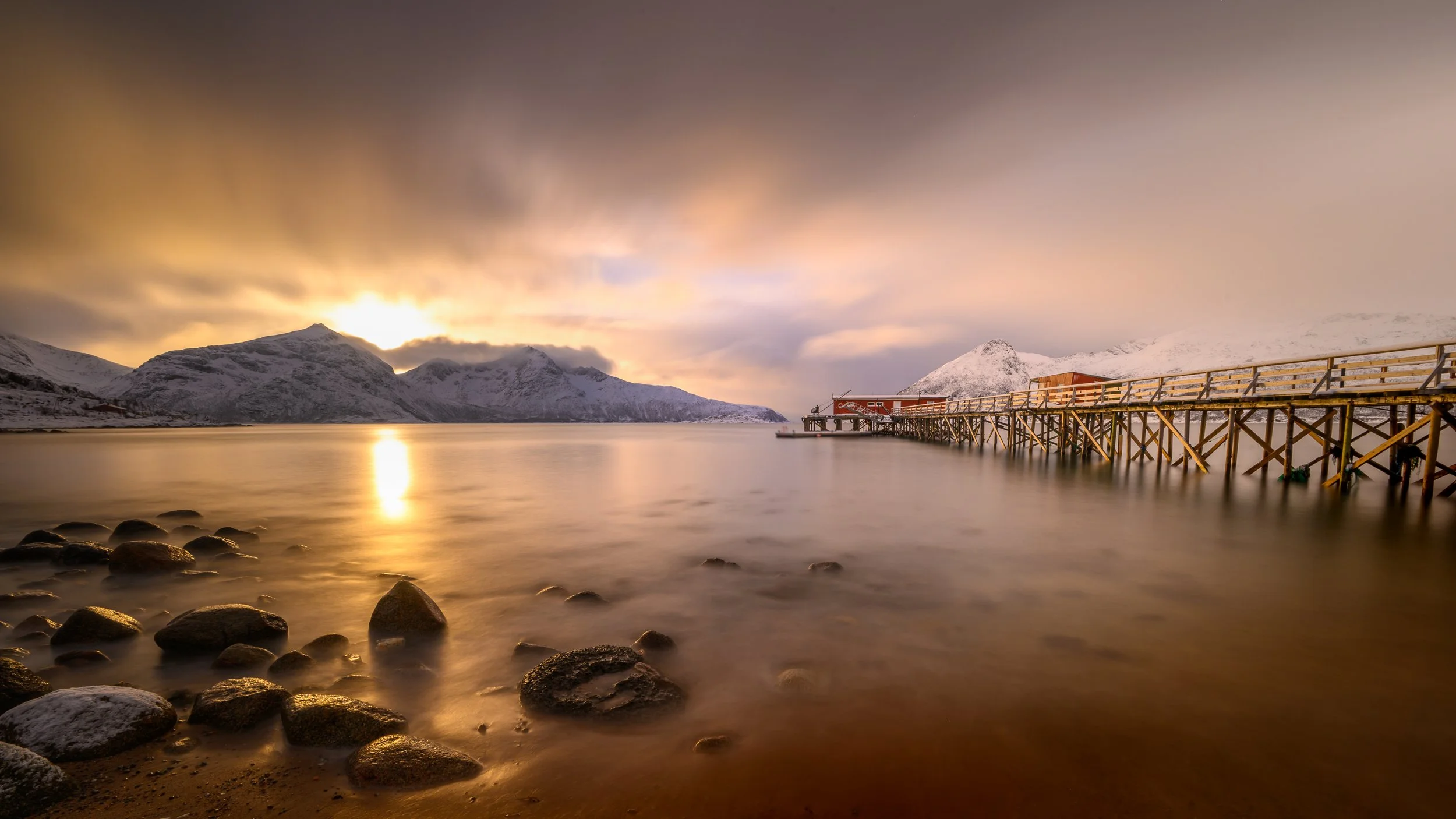 	Photographie de paysage nordique au coucher du soleil, ponton en bois sur un fjord calme sous une lumière dorée. Norvège