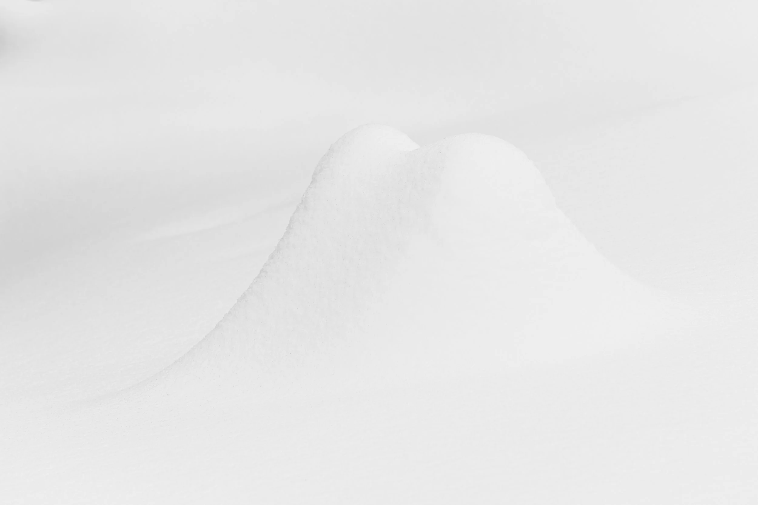 Deux monticules de neige arrondis se rejoignant, rappelant des formes sculpturales sur un fond blanc pur. Minimalisme