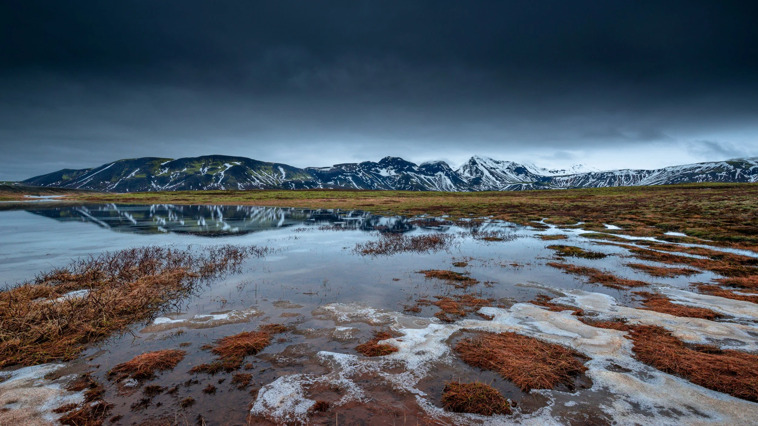 Paysage de toundra islandaise avec reflets dans les flaques d'eau sous un ciel sombre et menaçant, ambiance sauvage.