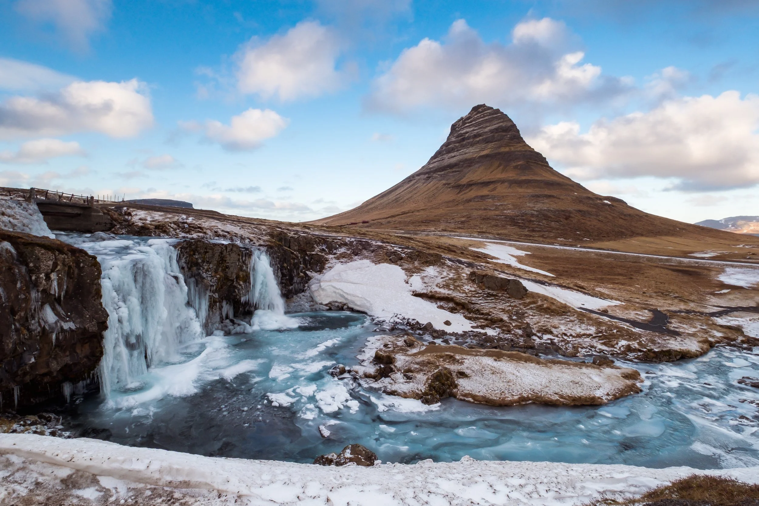 La montagne Kirkjufell et ses cascades partiellement gelées en hiver, paysage iconique d'Islande sous la neige.