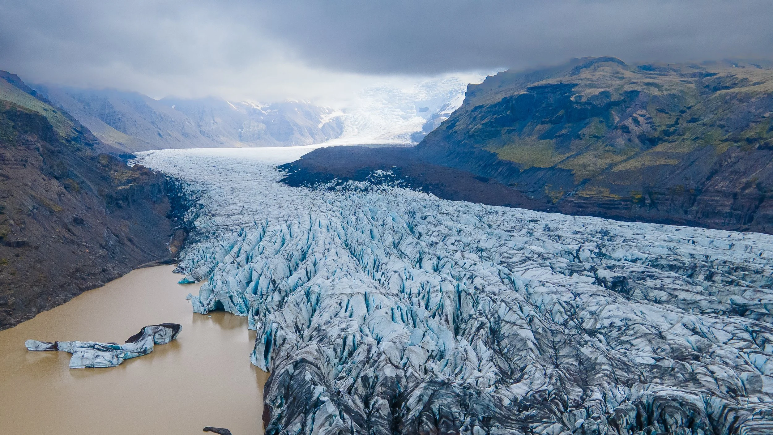  glace)	Vue aérienne d'une langue glaciaire serpentant dans une vallée minérale sombre, géologie et paysages du Grand Nord.  Islande