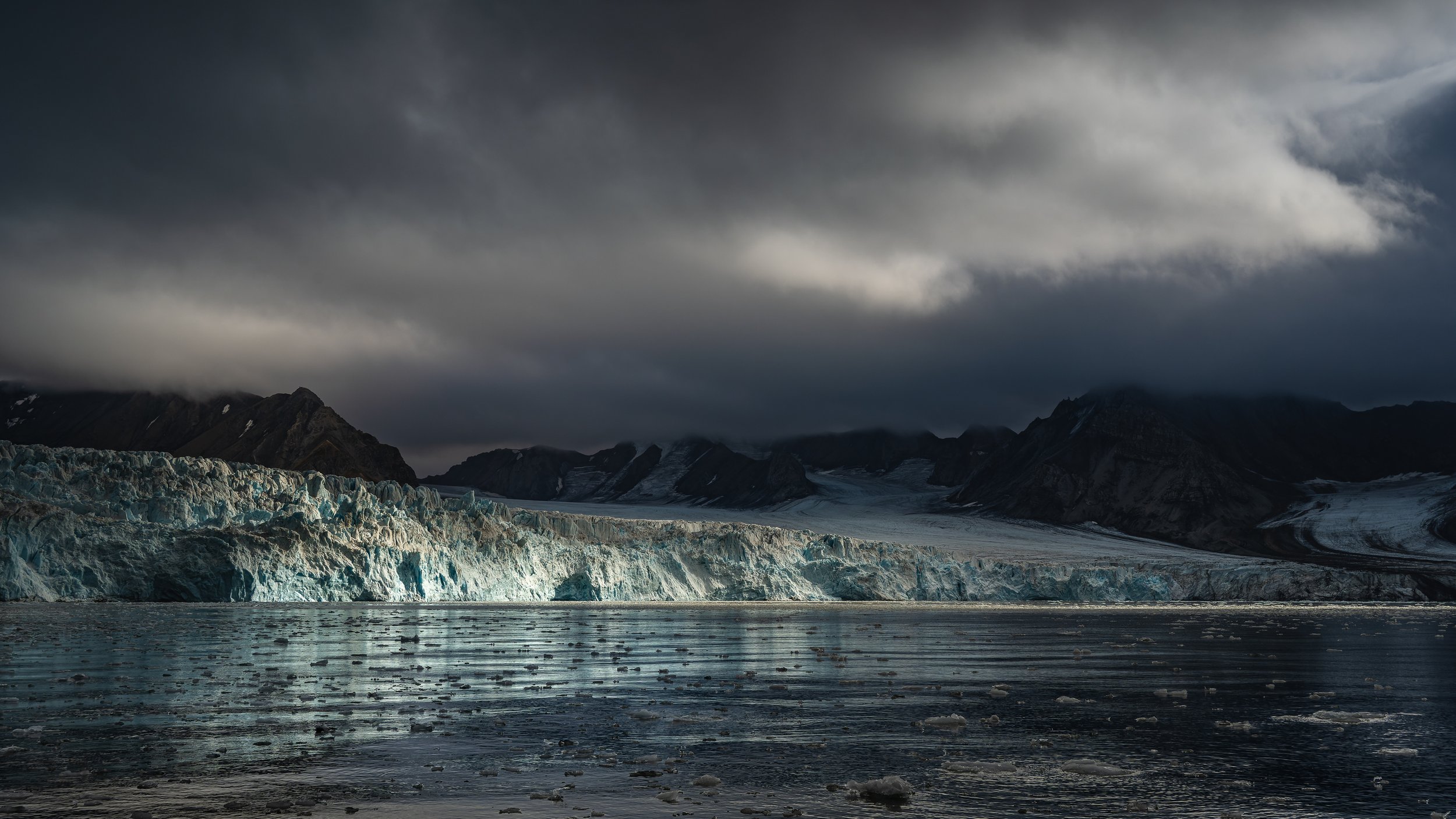 Panorama d'un front glaciaire massif se déversant dans l'eau sombre au pied de montagnes volcaniques, Spitsberg.