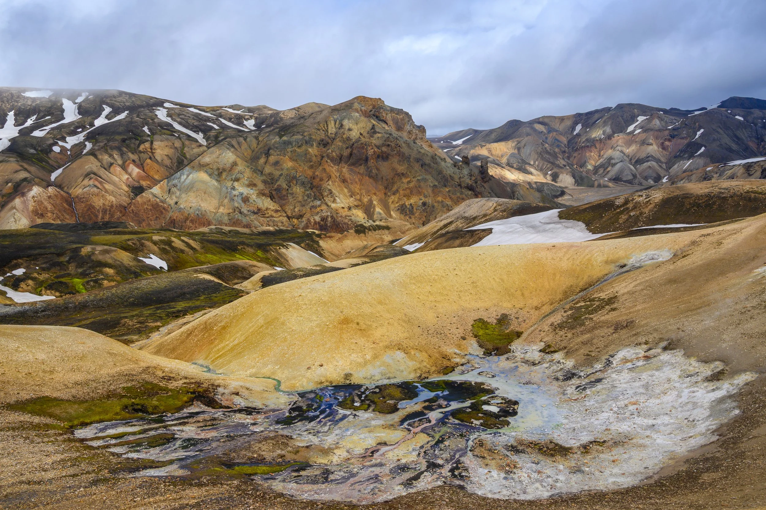 	Panoramique des montagnes de rhyolite aux couleurs ocre et pastel sous un ciel nuageux, cœur des hauts plateaux islandais.