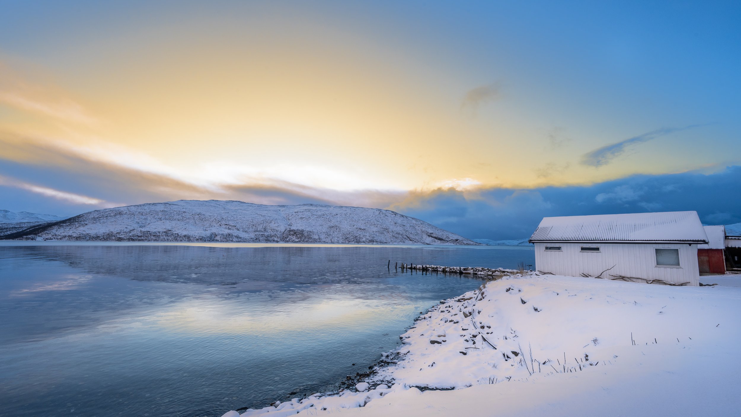 Maison rouge traditionnelle scandinave sous une lumière hivernale rase, paysage de neige et d'eau au lever du jour. Norvège