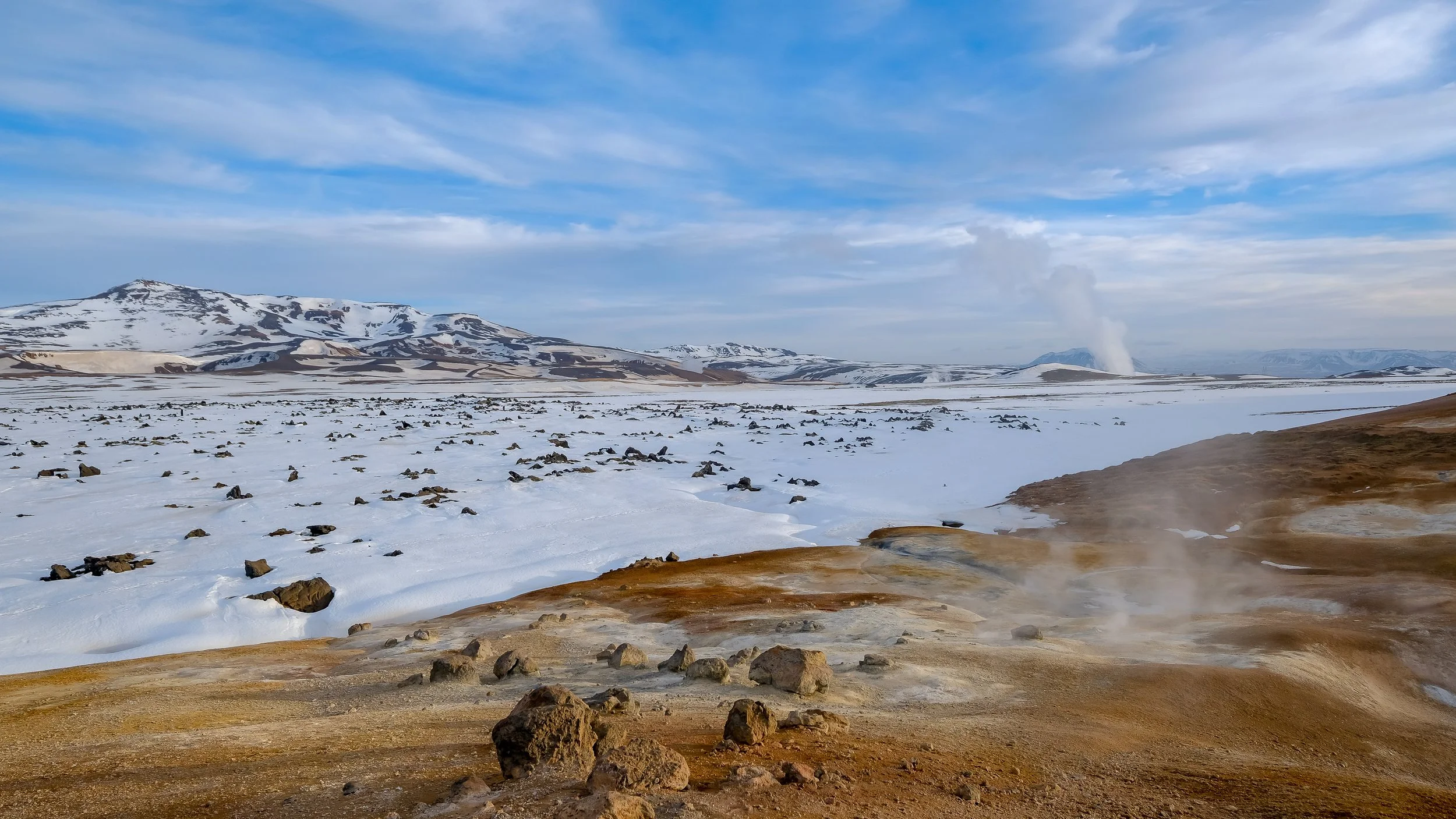 Vapeur volcanique s'élevant d'un sol ocre au milieu d'un désert de neige blanche, dualité entre feu et glace.