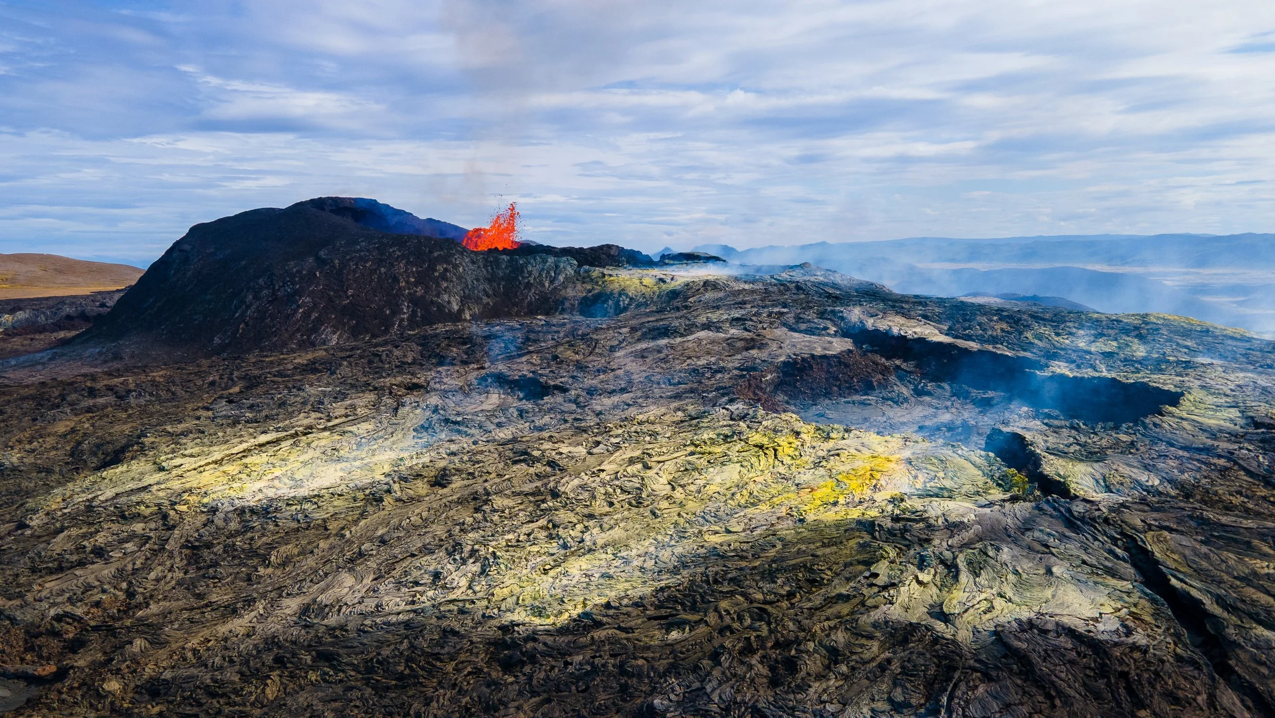 Vue aérienne d'une zone volcanique active avec coulée de lave sombre et fumerolles, force tellurique de l'Islande.