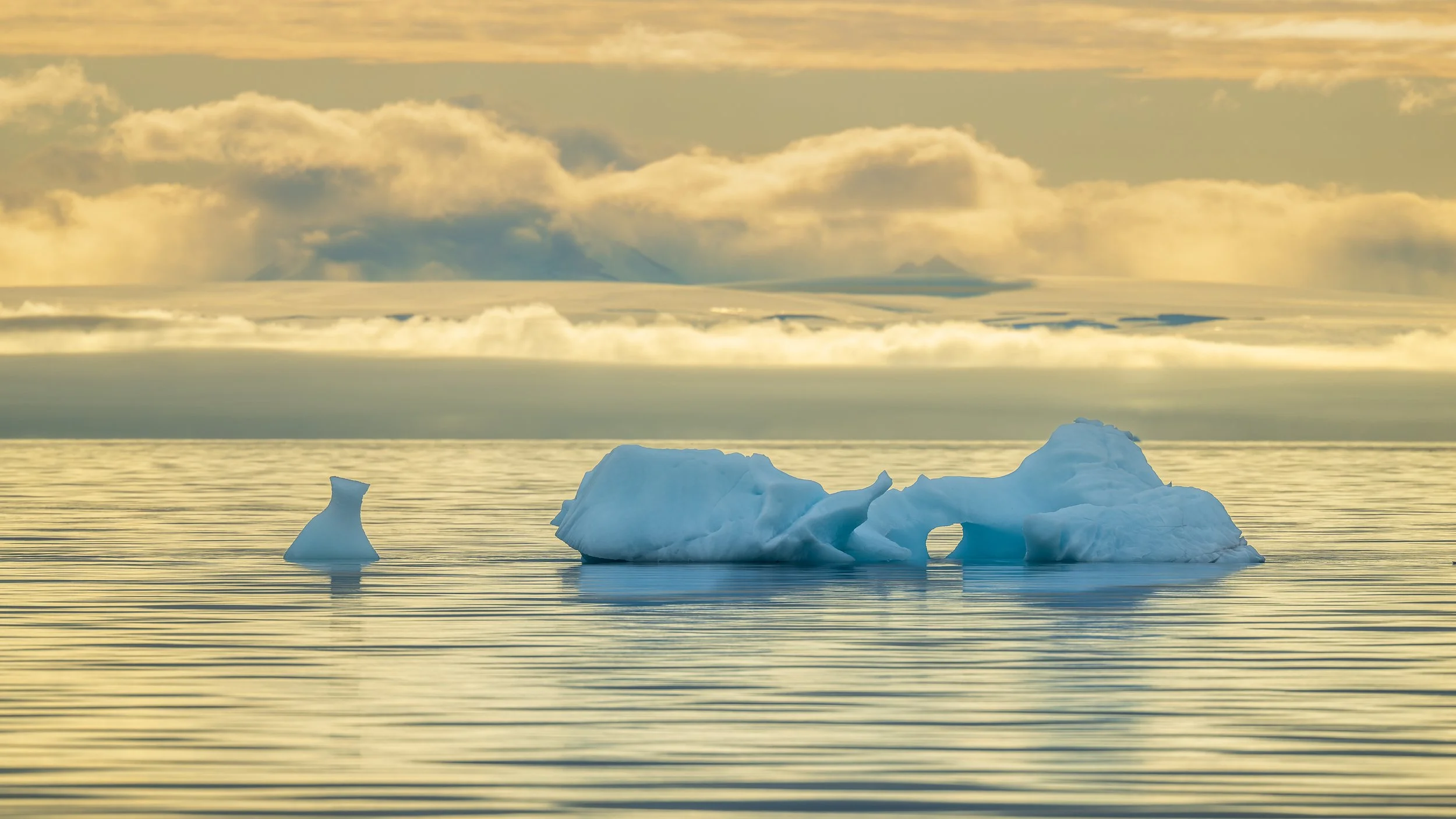 Fragments de glace dérivant sous une lumière dorée de fin de journée, contraste entre la froideur du cristal et la chaleur du ciel.