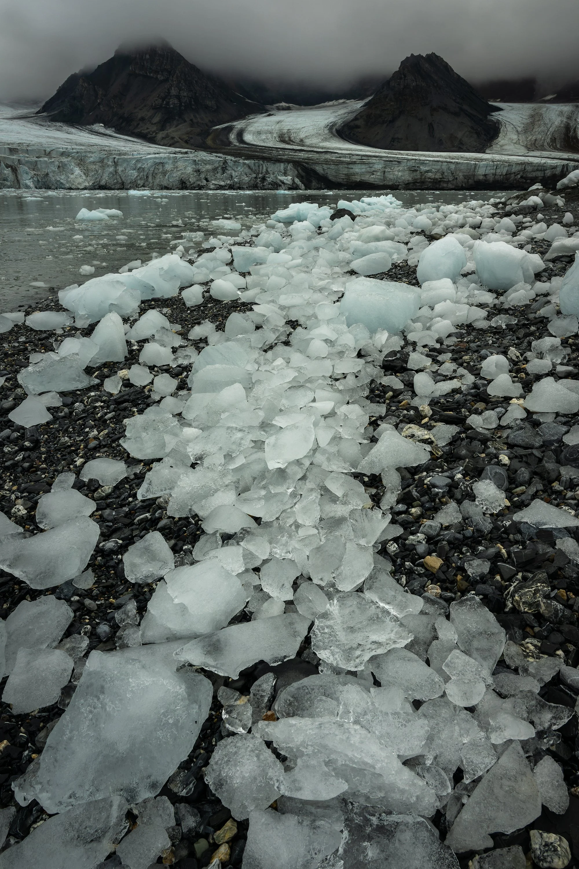 [Cadrage vertical] Détails de fragments de glace accumulés formant une ligne directrice vers des sommets brumeux, texture et matière. Spitsberg