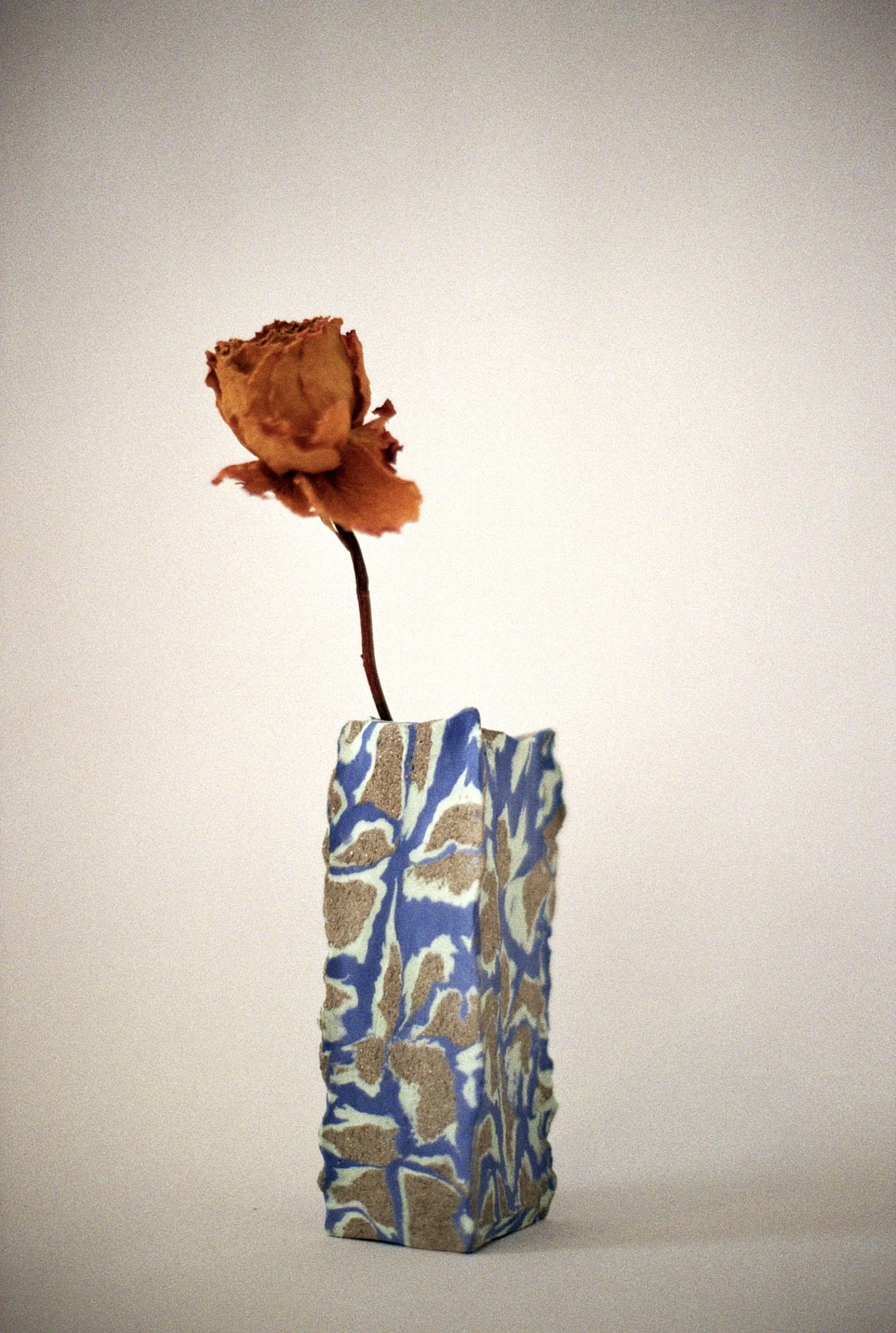 A dried orange rose in a mottled blue and beige ceramic vase.