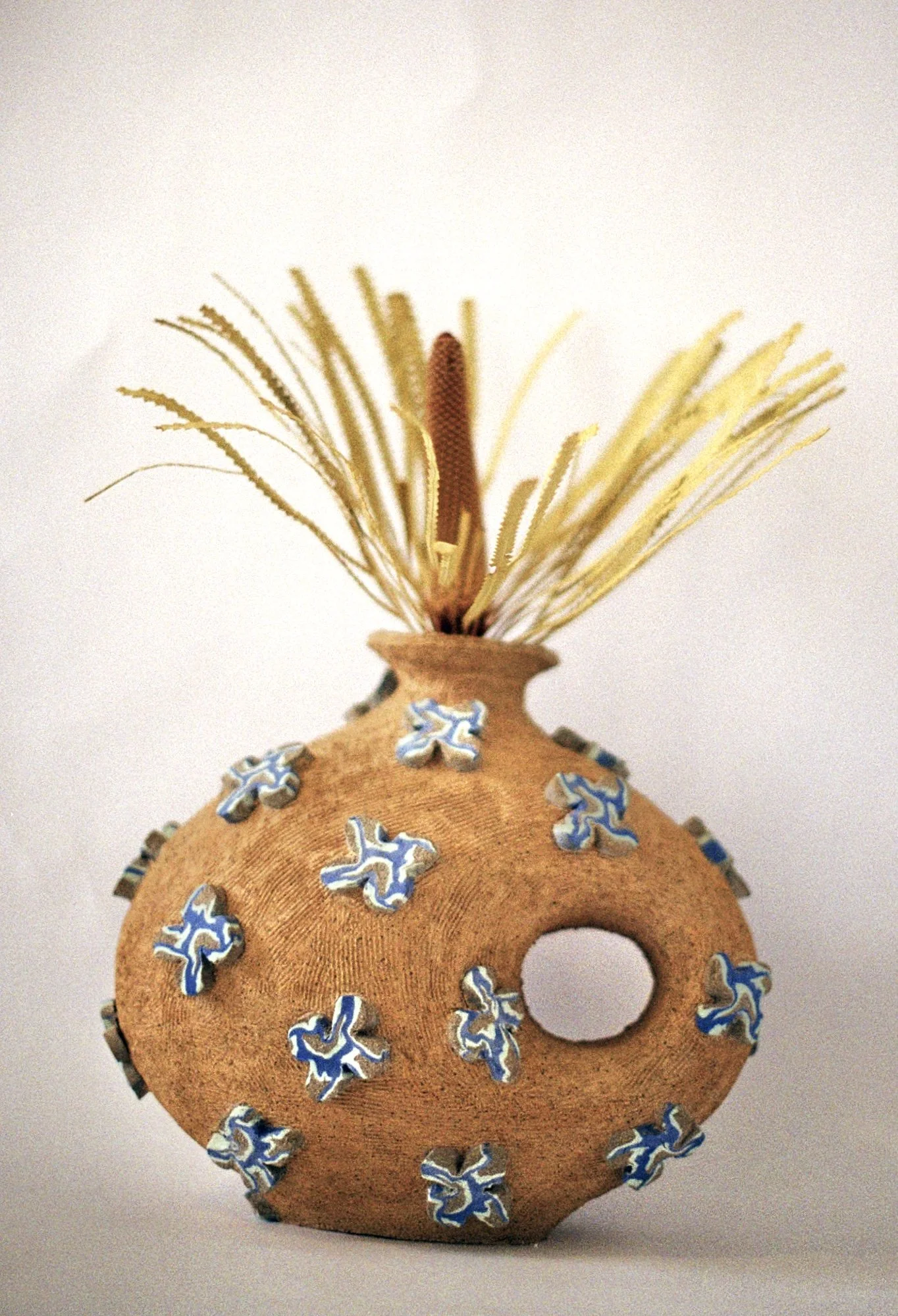 Decorative ceramic vase with blue and white floral designs, filled with dried flowers and grass, on a plain background.