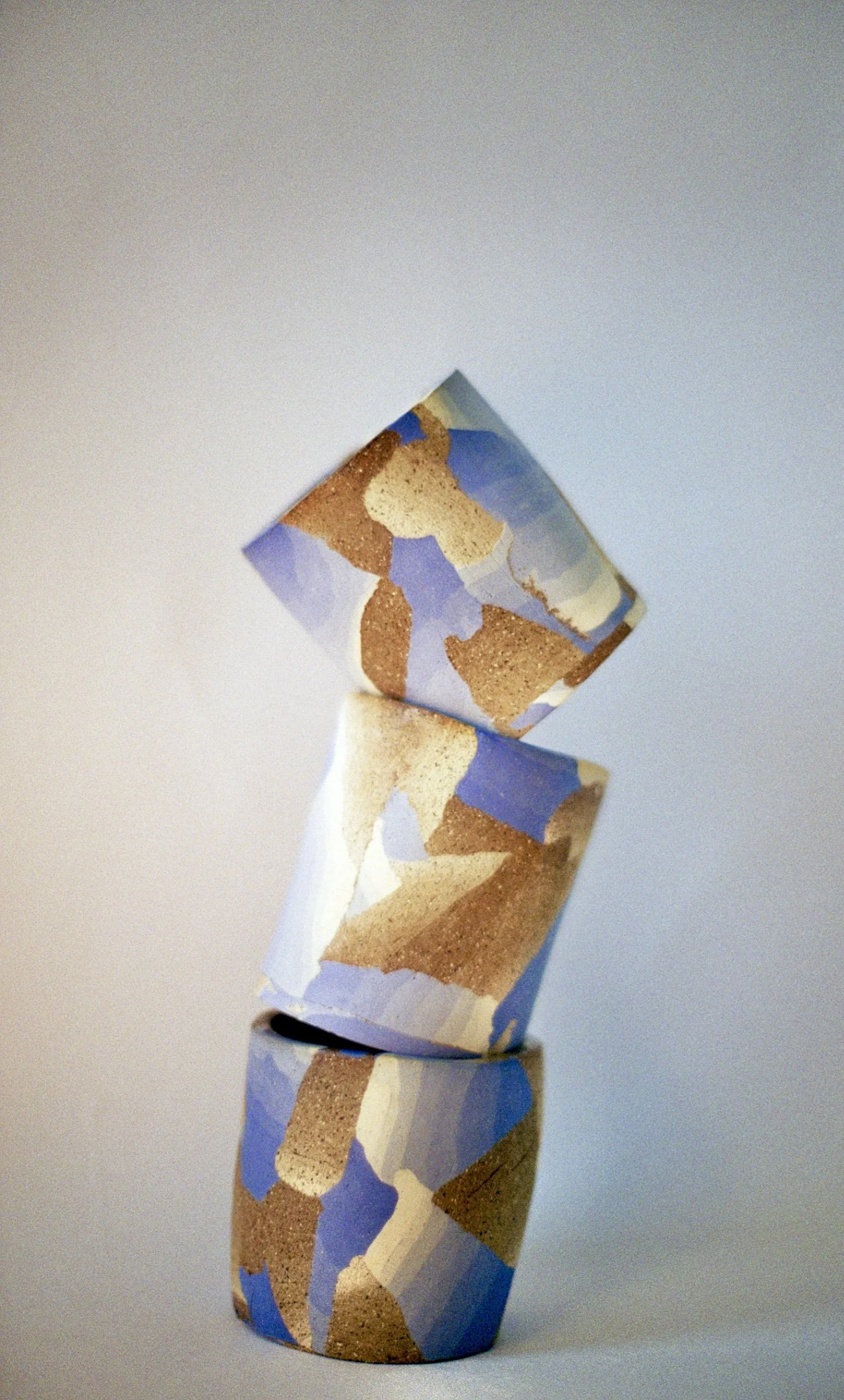 Three small cylindrical objects with a colorful abstract pattern, stacked one on top of the other, against a plain background.