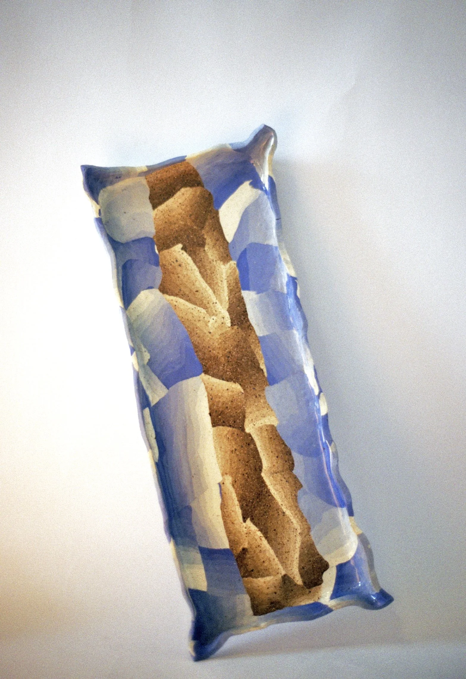 A crumpled, colorful plastic wrapper with a design resembling broken pieces of bread and blue abstract shapes on a plain white surface.