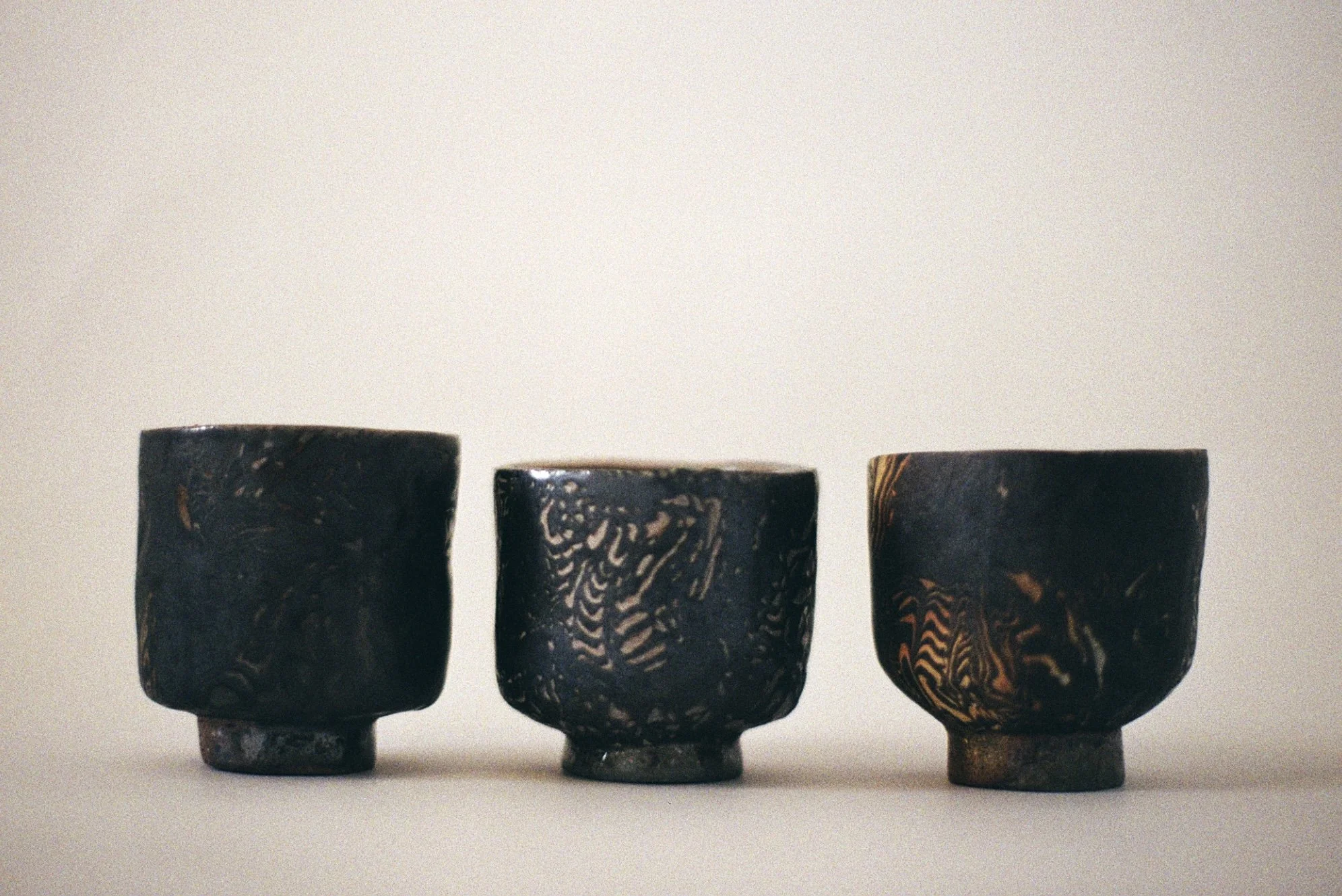 Three black ceramic cups with marbled patterns, placed side by side on a plain surface against a light background.