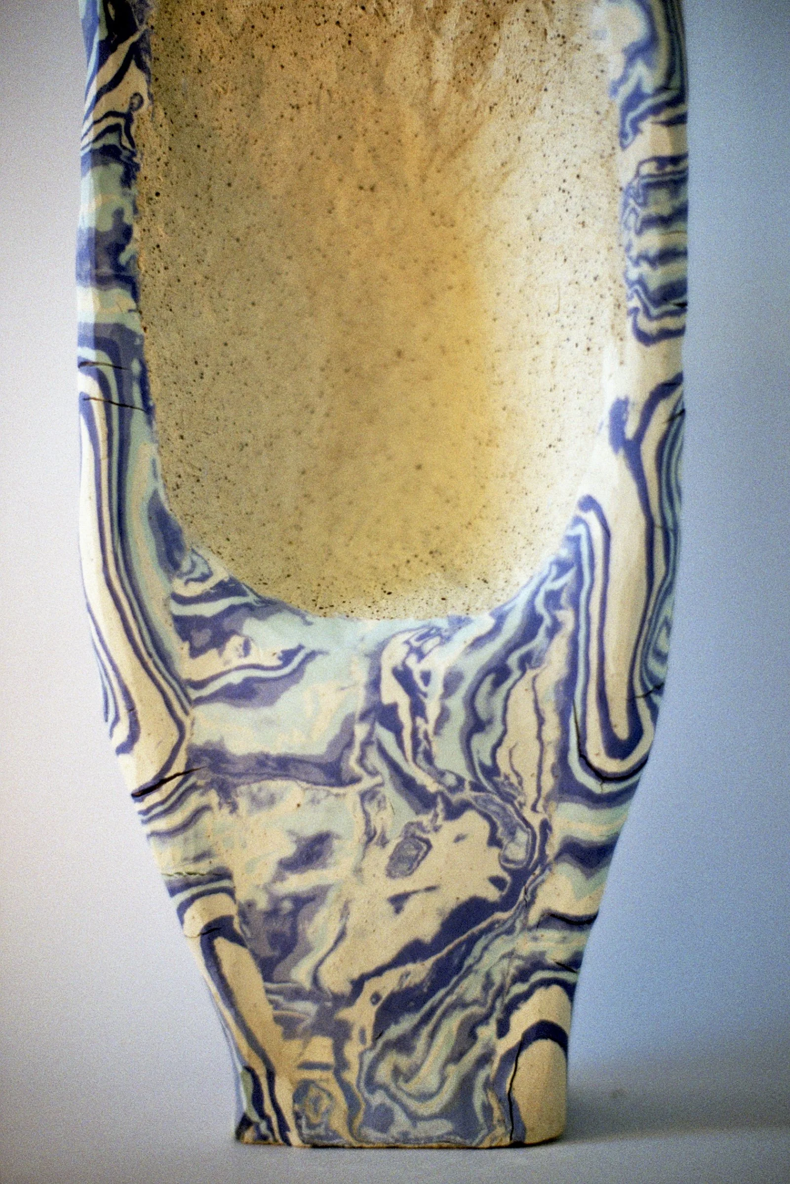 A ceramic vase with a marbled design in blue, white, and beige, featuring an oval-shaped opening at the top