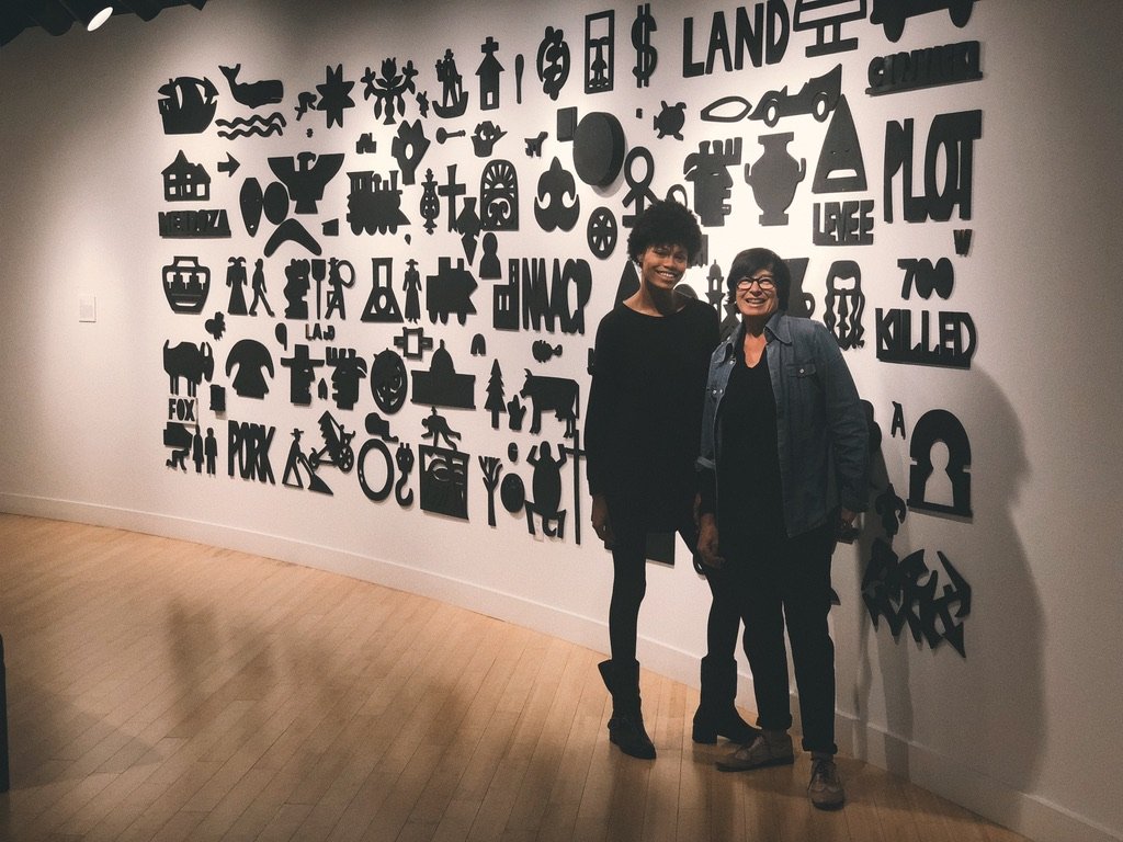 ming and former Lubeznik Center for the Arts Curator, visual artist, Lora Fosberg posed in front of artwork by Bernard Williams on view at LCA in the 2018 exhibition "Waiting For A Sign."
