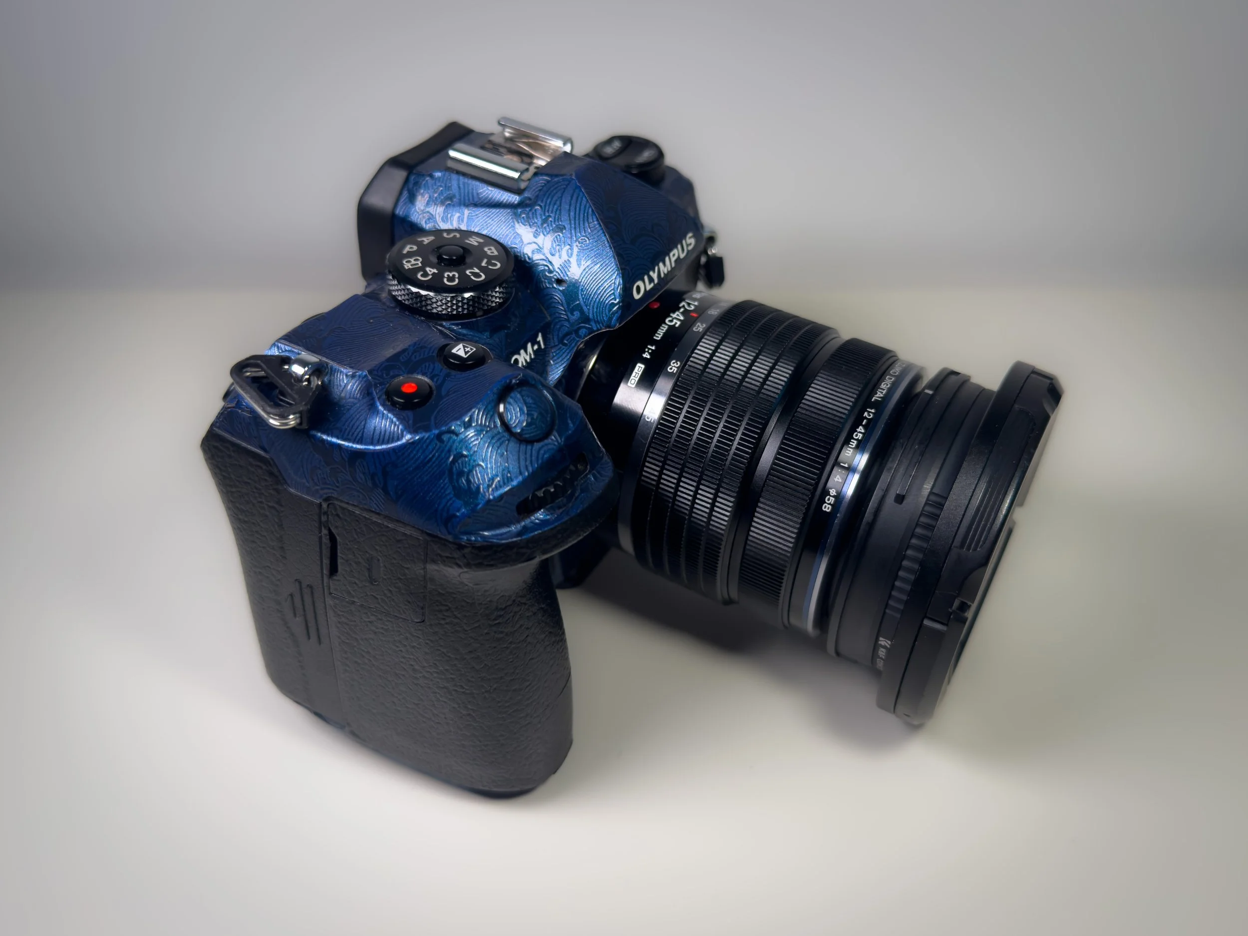 A digital camera with a blue patterned body and a black lens, placed on a white surface.