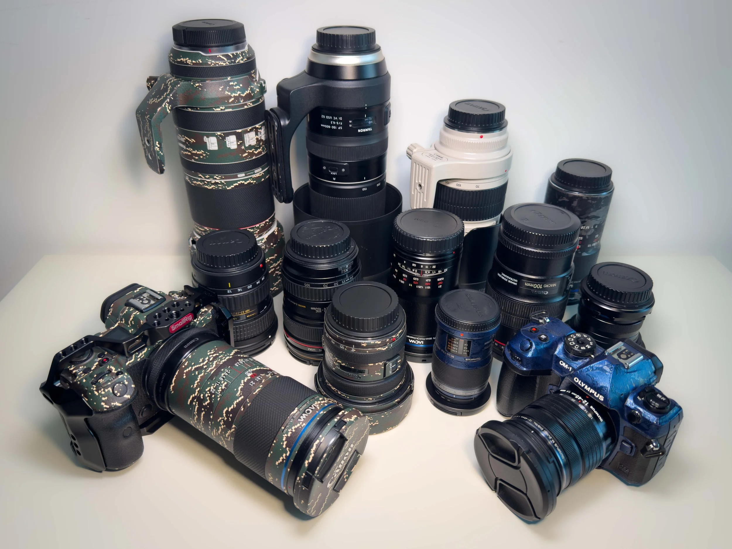 Collection of professional cameras and lenses, including a camera with a camouflage pattern, a blue camera, and multiple lenses of various sizes.