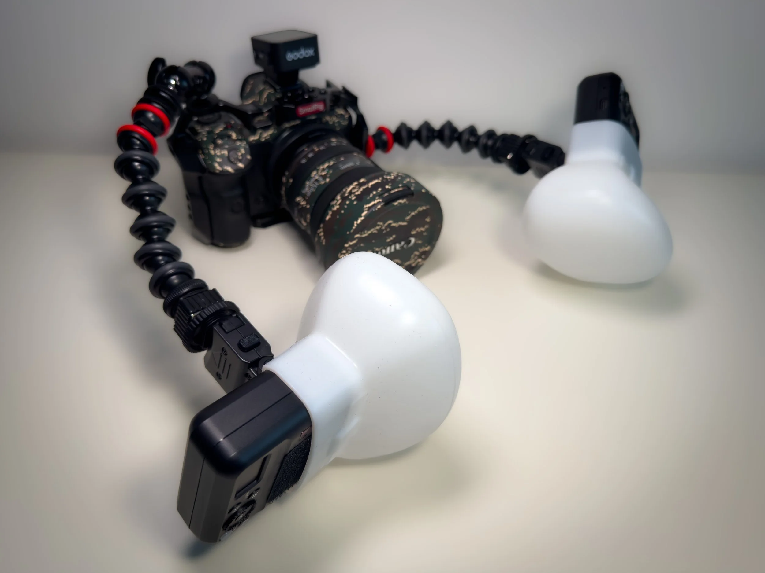 Camera with a lens and a softbox light attached, mounted on a flexible arm, on a white surface