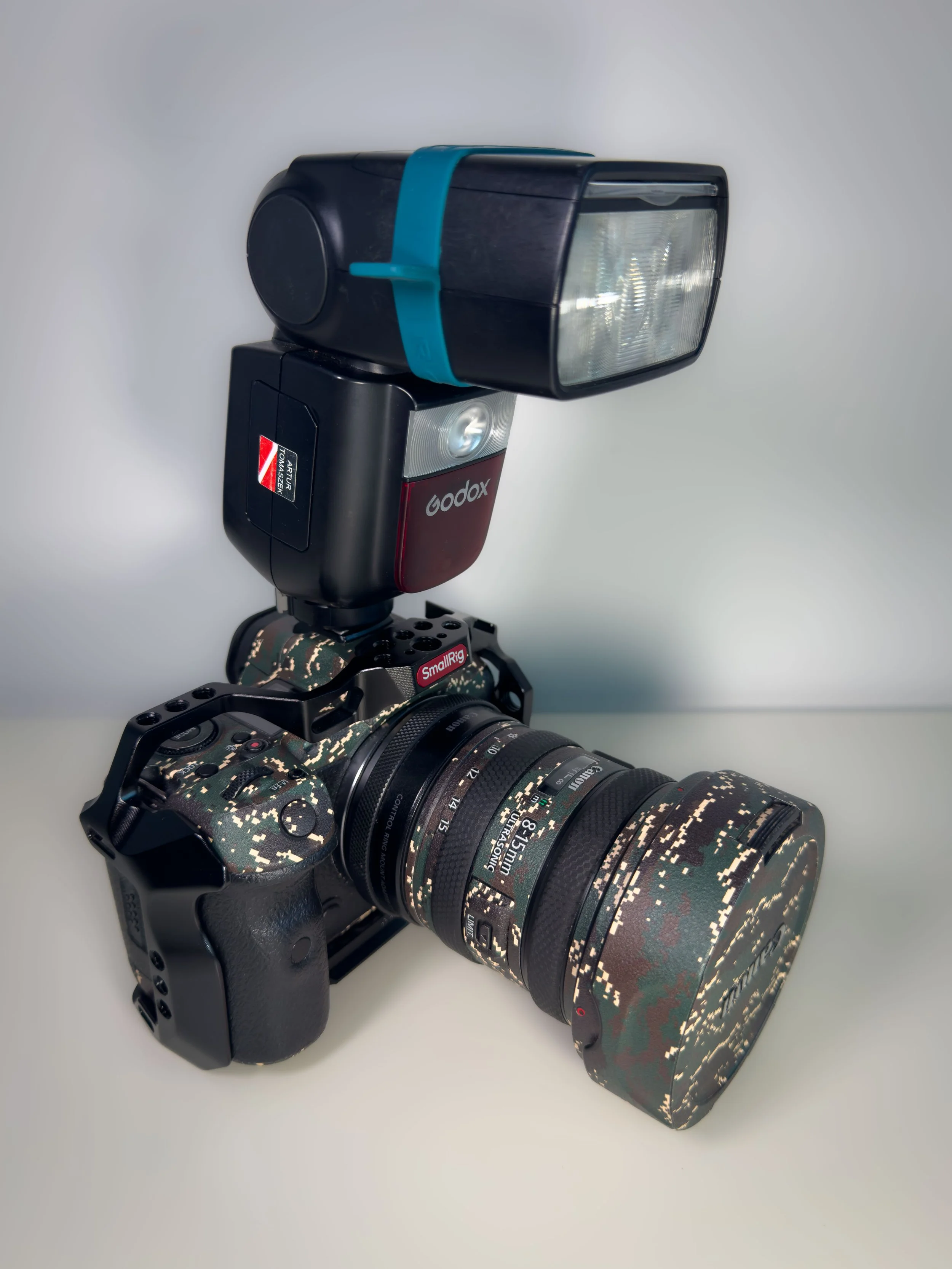 A camera with a camouflage pattern lens, mounted with a flash and a Godox external flash unit attached to it.