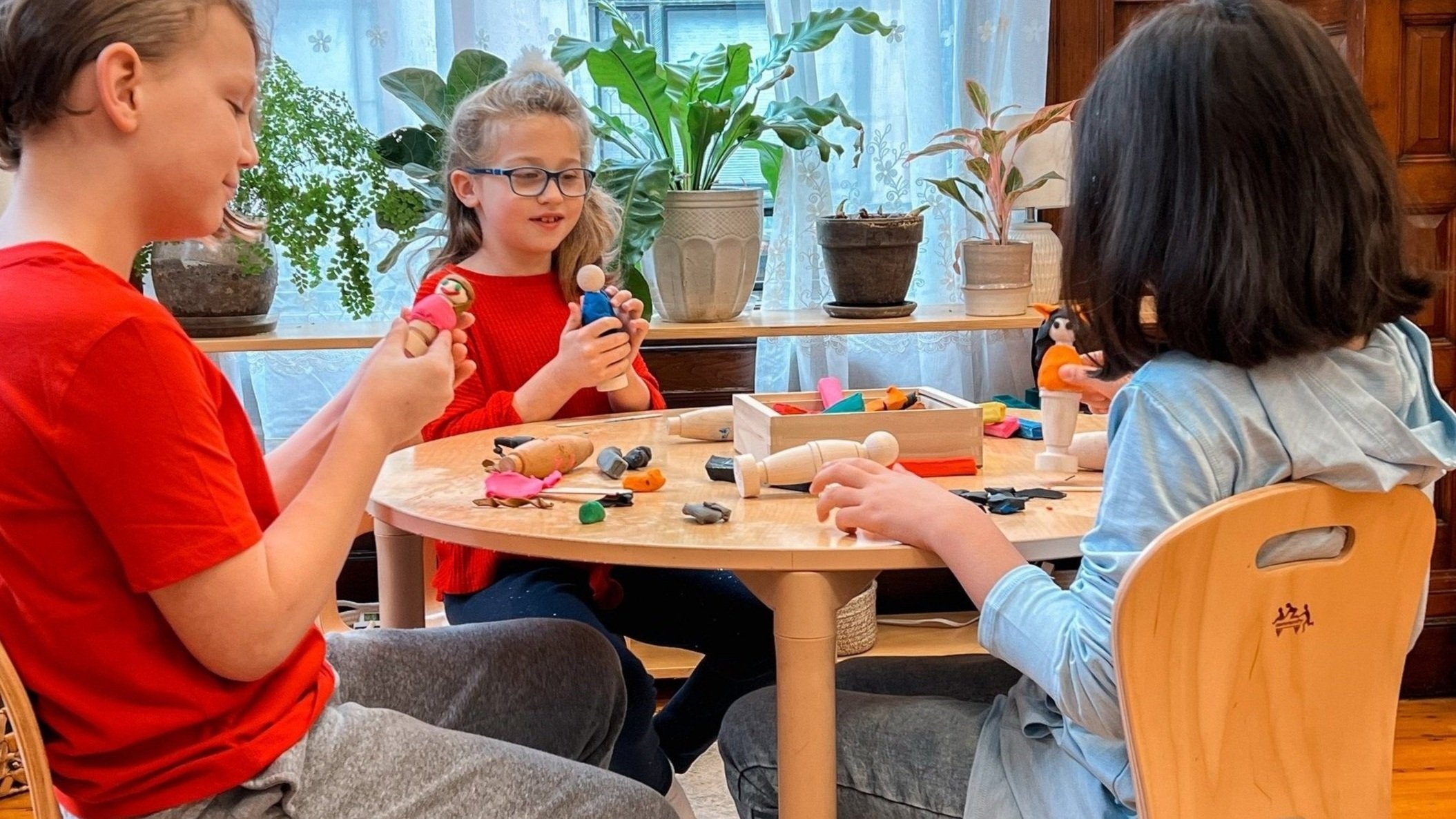 Photo of 3 children playing with wooden figures and clay.